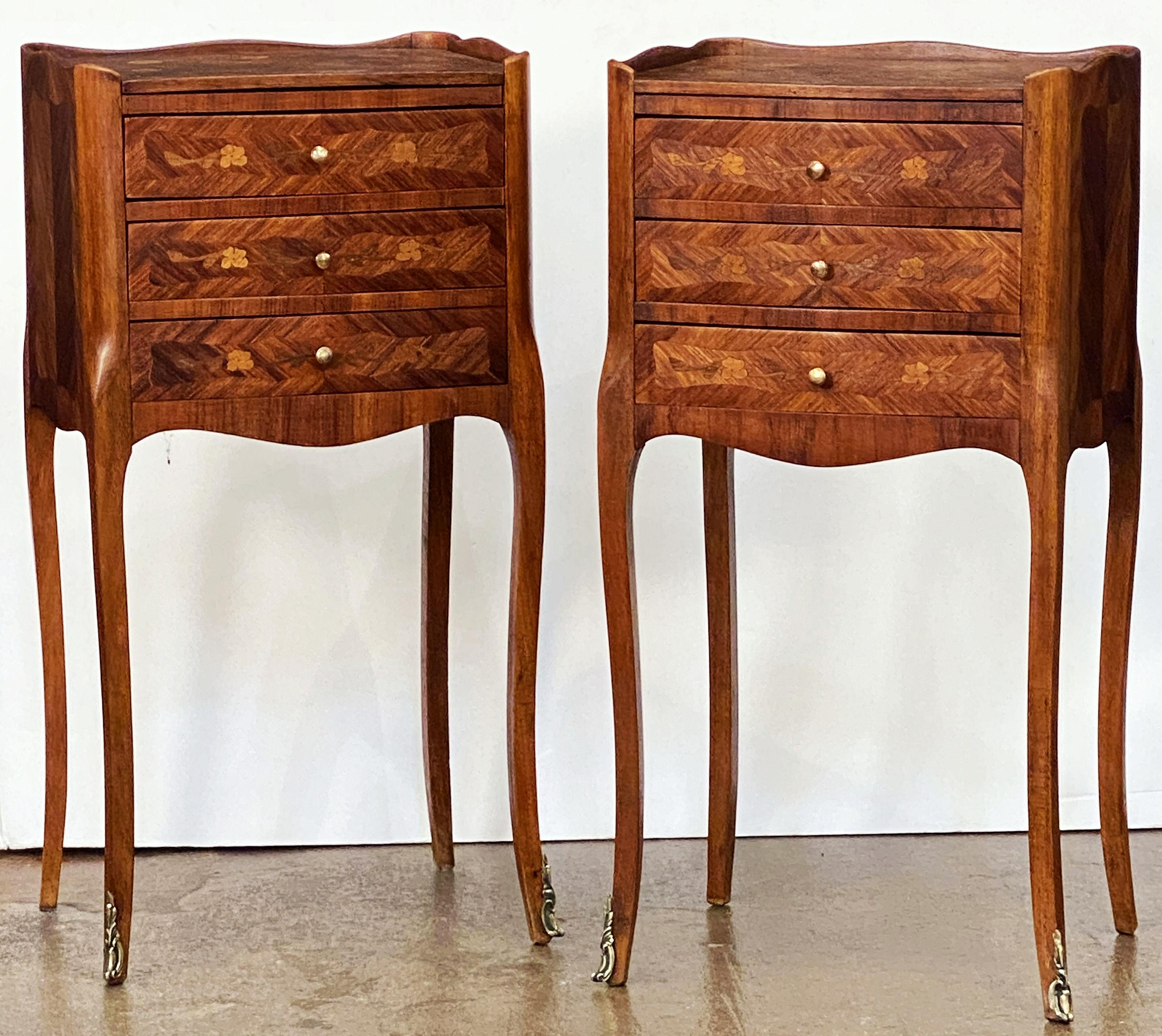 A fine pair of French bedside end tables or nightstands, each stand featuring an inlaid top with serpentine gallery over a frieze of three inlaid drawers with brass pulls, marquetry sides and apron bottom, and set upon four cabriole legs with ormolu
