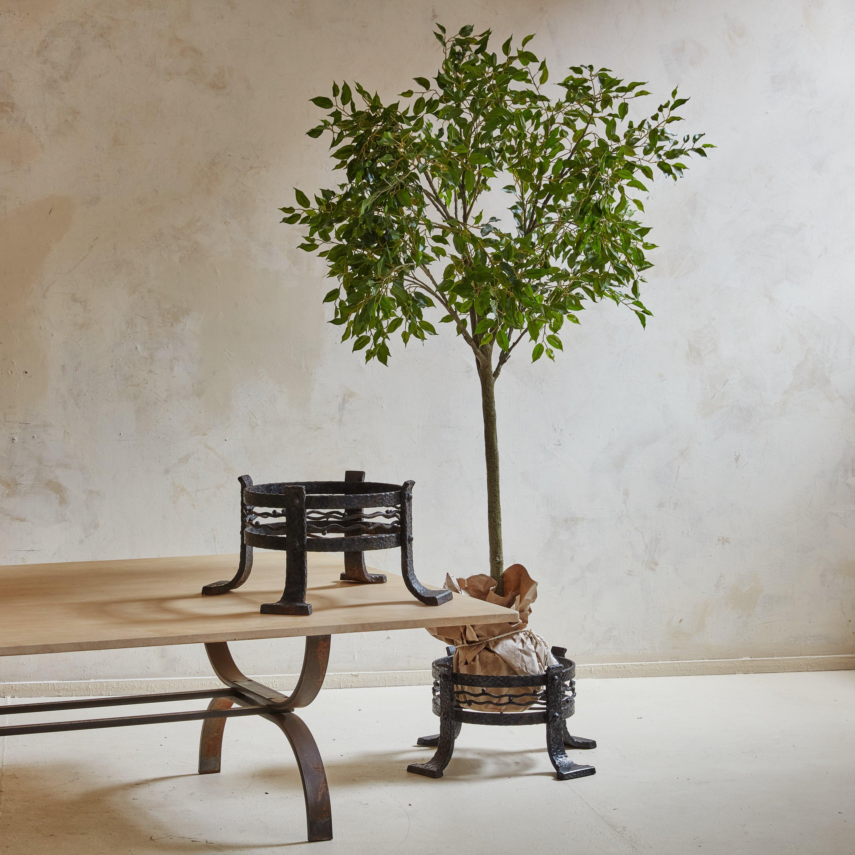 A pair of French iron plant stands from the 1920s, which show a beautiful example of French artisanal ironwork. 

 The circular silhouettes feature squiggle motifs and four legs with oversized feet. The textured surface has aged beautifully over