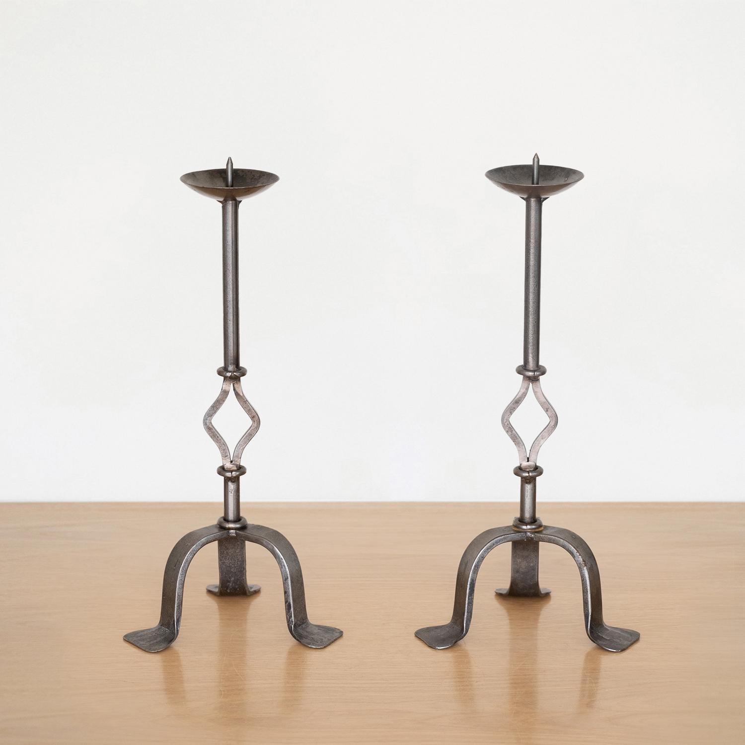 Great pair of decorative iron candlesticks from France. Single stems with ornate detailing and tripod base. Original light metal finish with some age and wear. Sold as a pair.