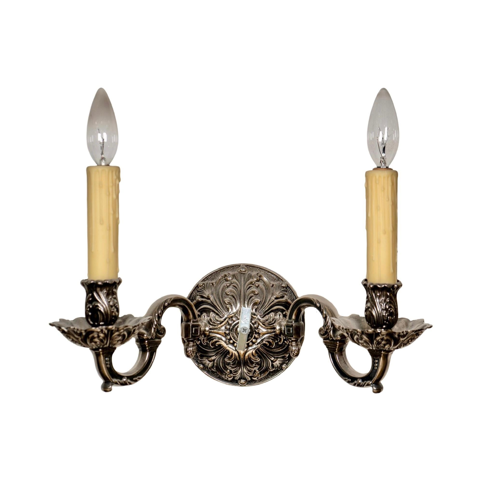 Fabricados a mano en Francia en la década de 1950, estos apliques de hierro francés presentan un motivo floral único que añade elegancia y encanto a cualquier habitación. Cada candelabro tiene dos apliques de luz, que proporcionan una iluminación