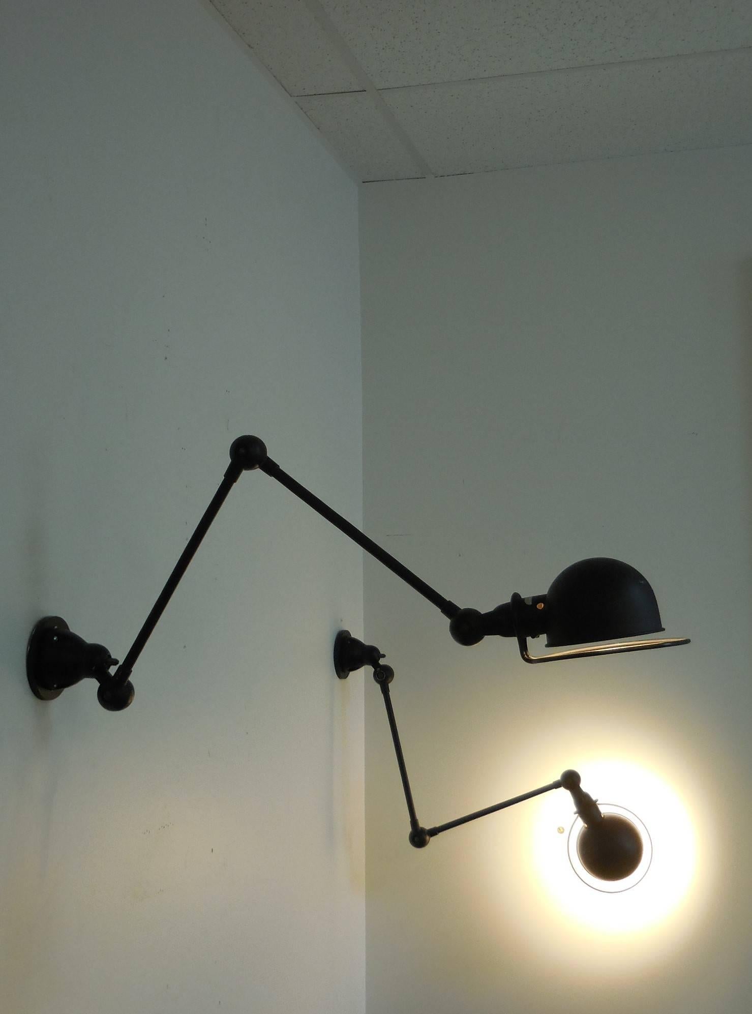 A pair of adjustable arm sconces. There are three articulated joints that allow the arms to be extended in multiple configurations, keep in mind that the diffuser also rotates. Black enamel finish. Retain original wall mounting plates. Original