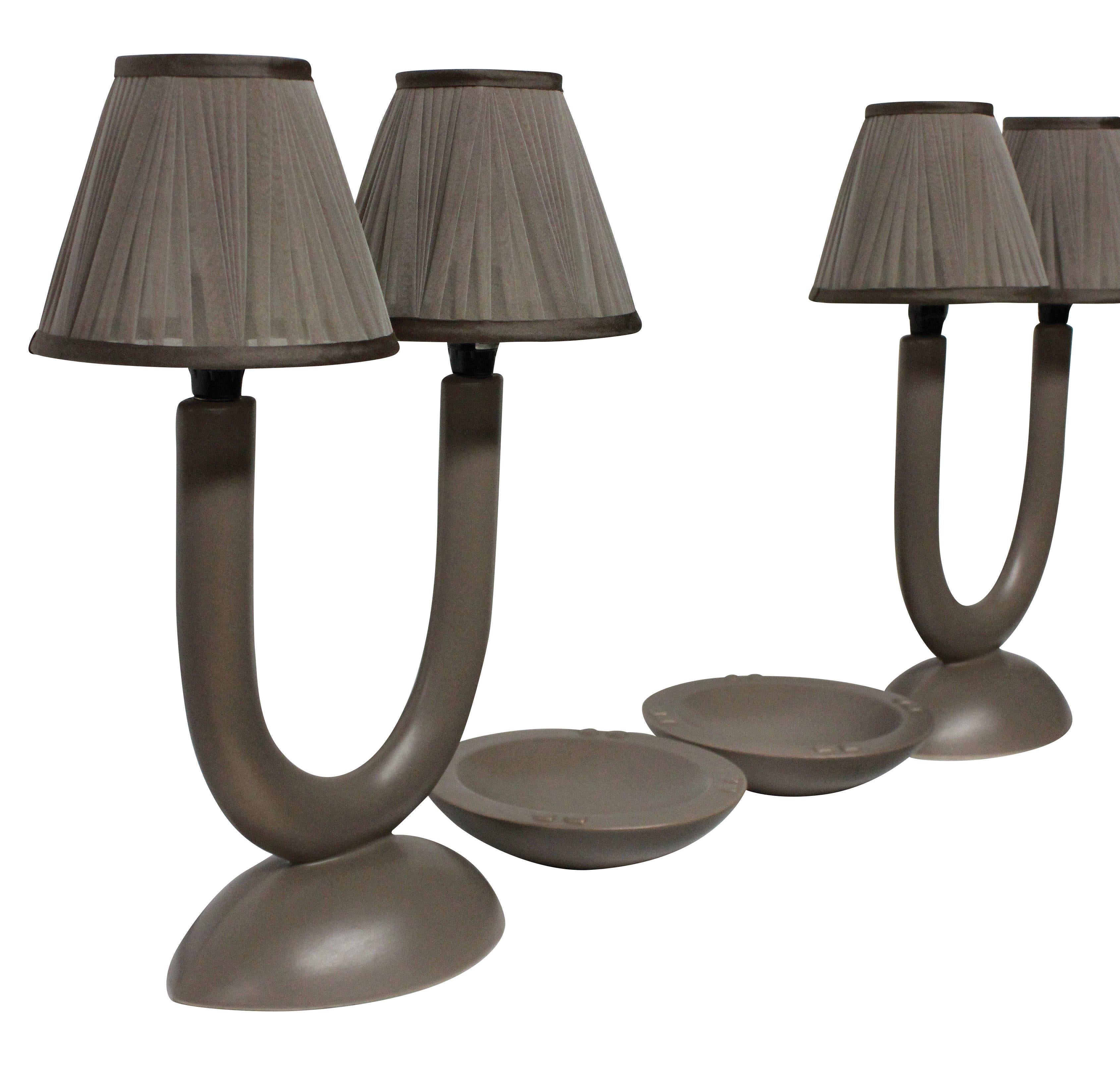 A pair of stylish French bisque porcelain lamps and matching ashtrays in a stone color with new pleated shades.