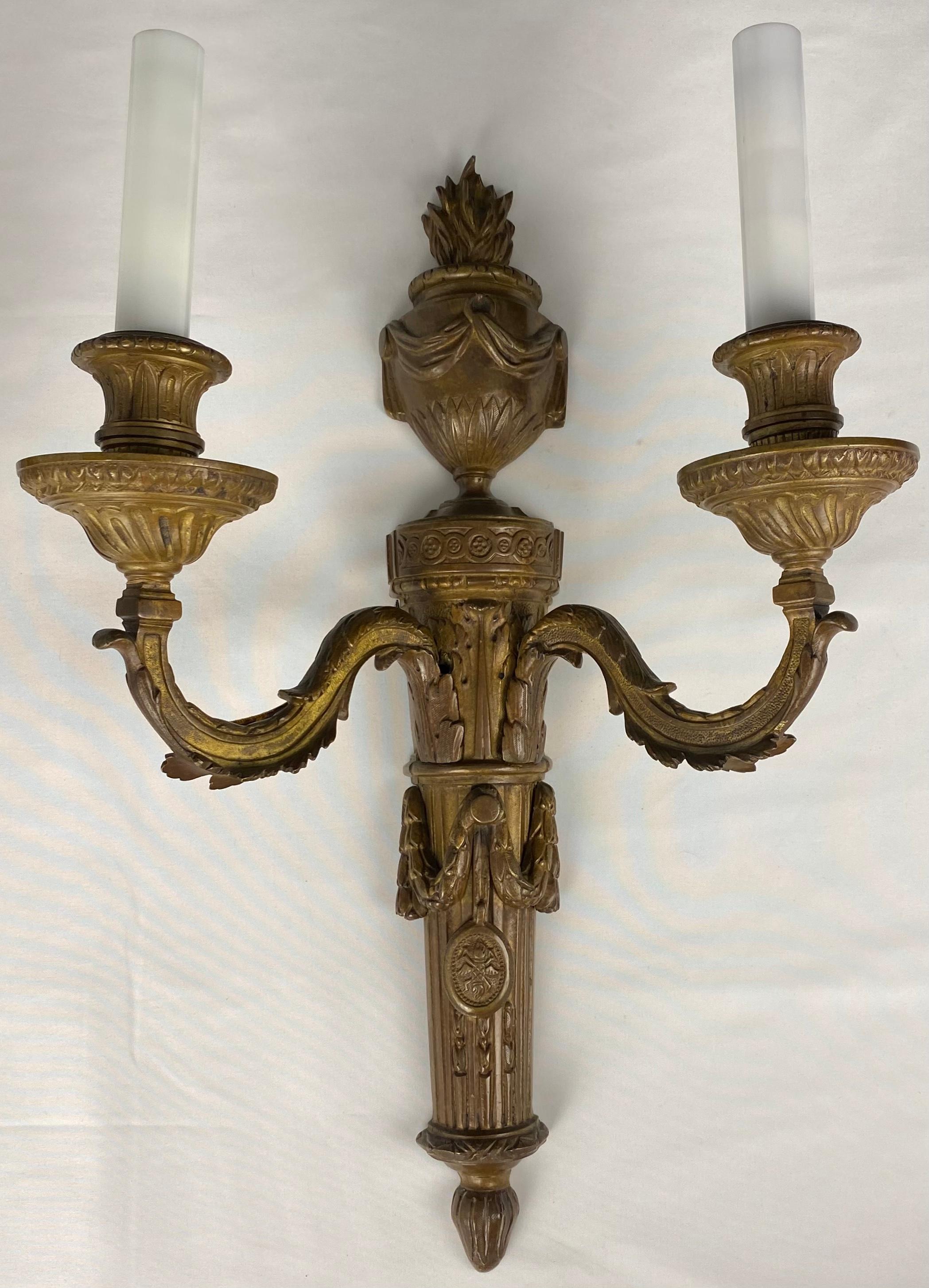 A fine quality pair of French late 18th century Louis XVI gilt bronze sconces. The two S scrolled arms have been electrified, details include a flamed torch signifying strength and prosperity, tied with a ribbon. Above is a reeded urn design with a