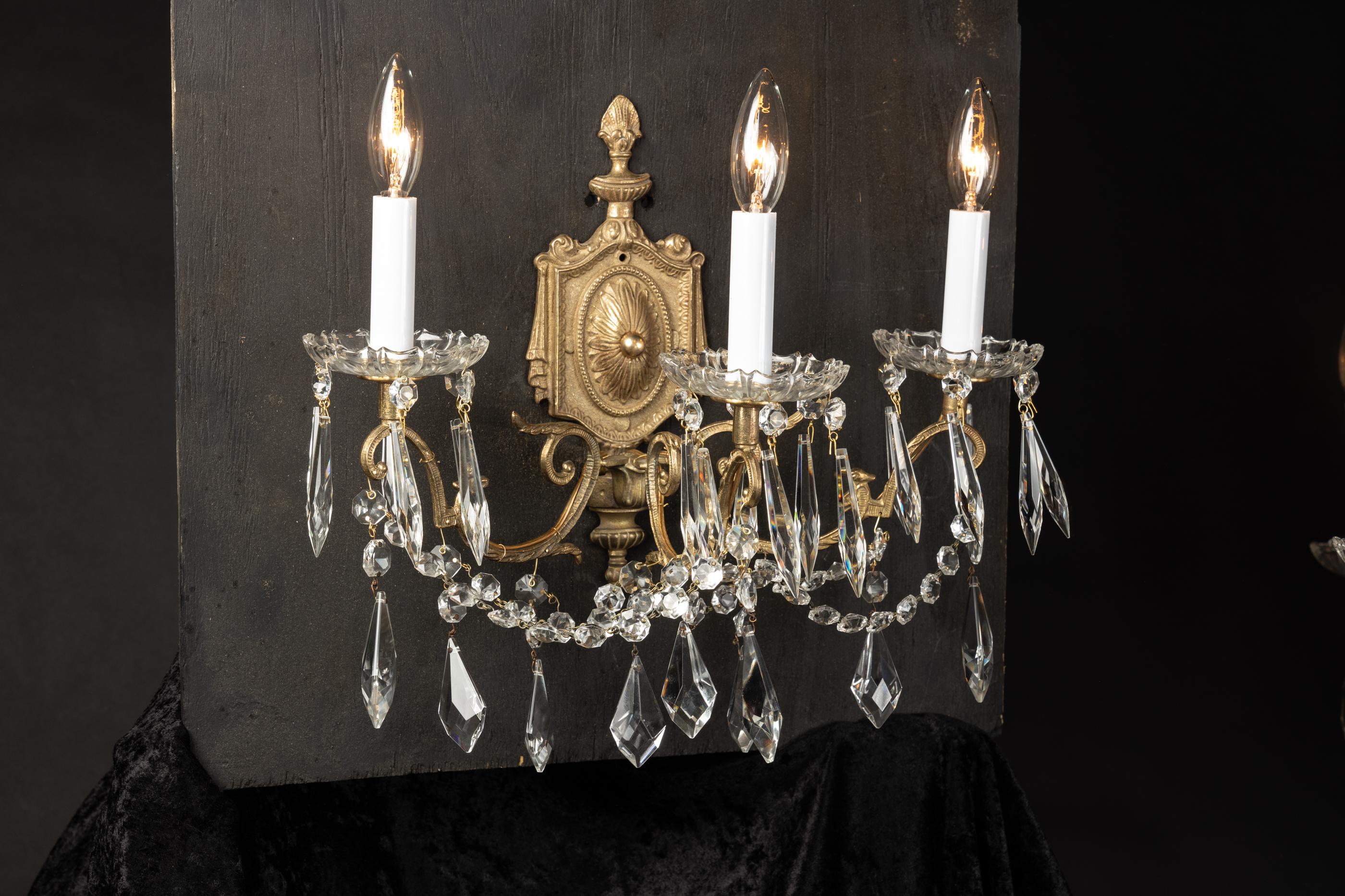 This beautiful pair of Louis XVI style French antique sconces feature three arms each as well as crystal bobeches. The pair dates back to the late 19th century. The arms are draped in octagonal crystal, crystal spears, and simple plaquettes. The