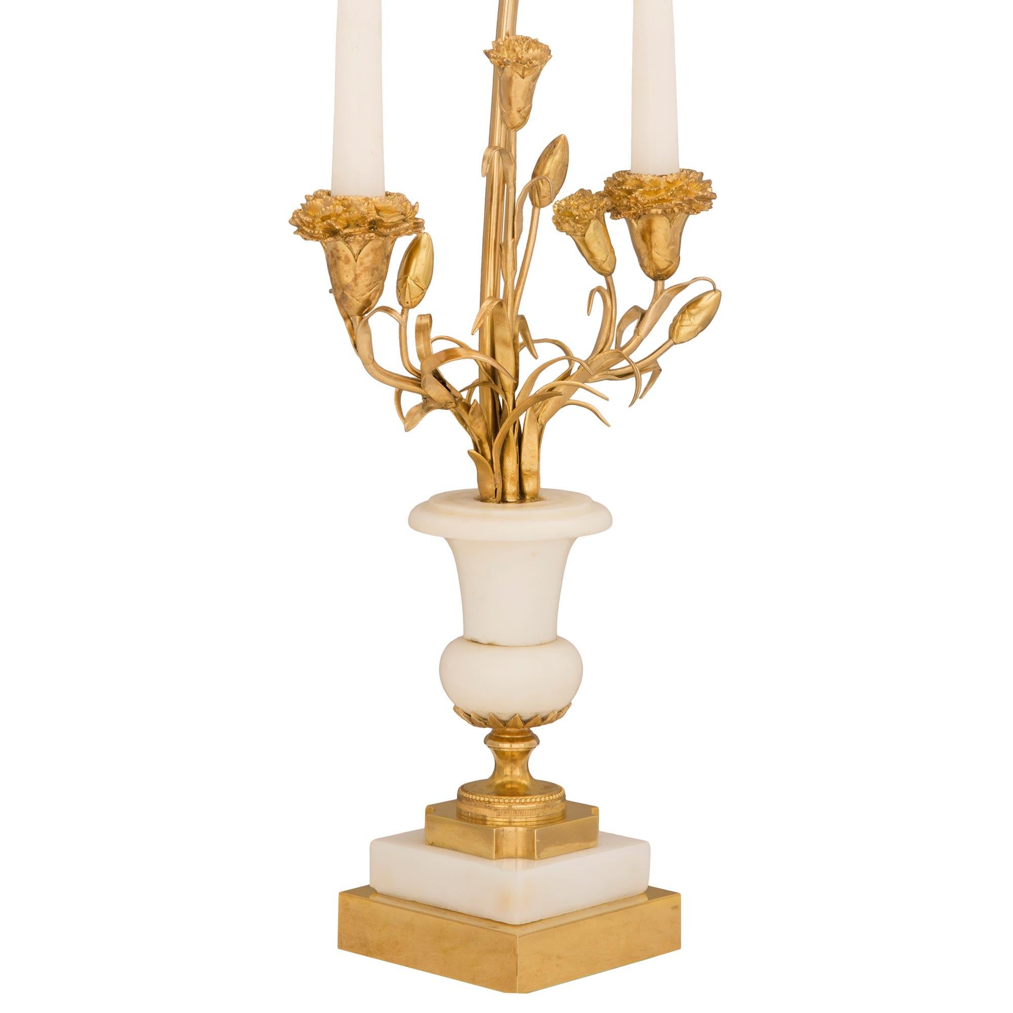 An exquisite pair of French late 19th century Louis XVI st. ormolu and white Carrara marble candelabras lamps. Each lamp is raised by a square ormolu base with fine bun feet below the socle shaped pedestal with wrap around beaded bands and cut