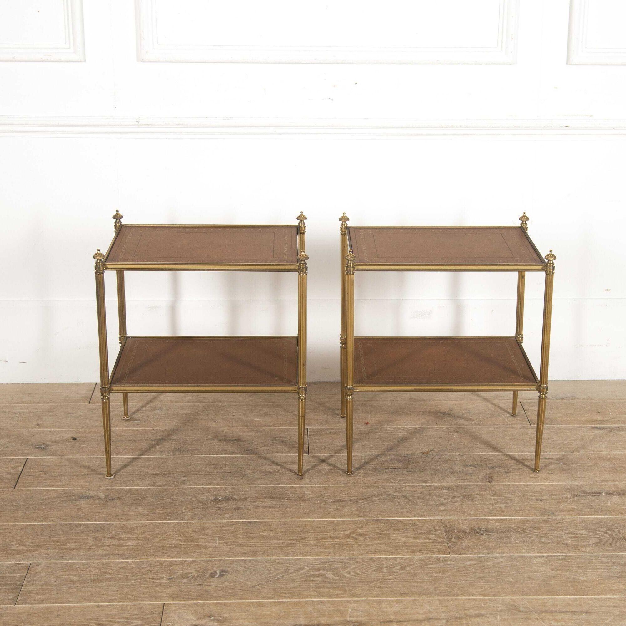 Elegant pair of French neoclassical side tables, circa 1960. 
These stylish tables feature two gilt-tooled tan leather rectangular tiers. The shelves are supported within an elegant brass framework. Decorative finials adorn the tops of the four