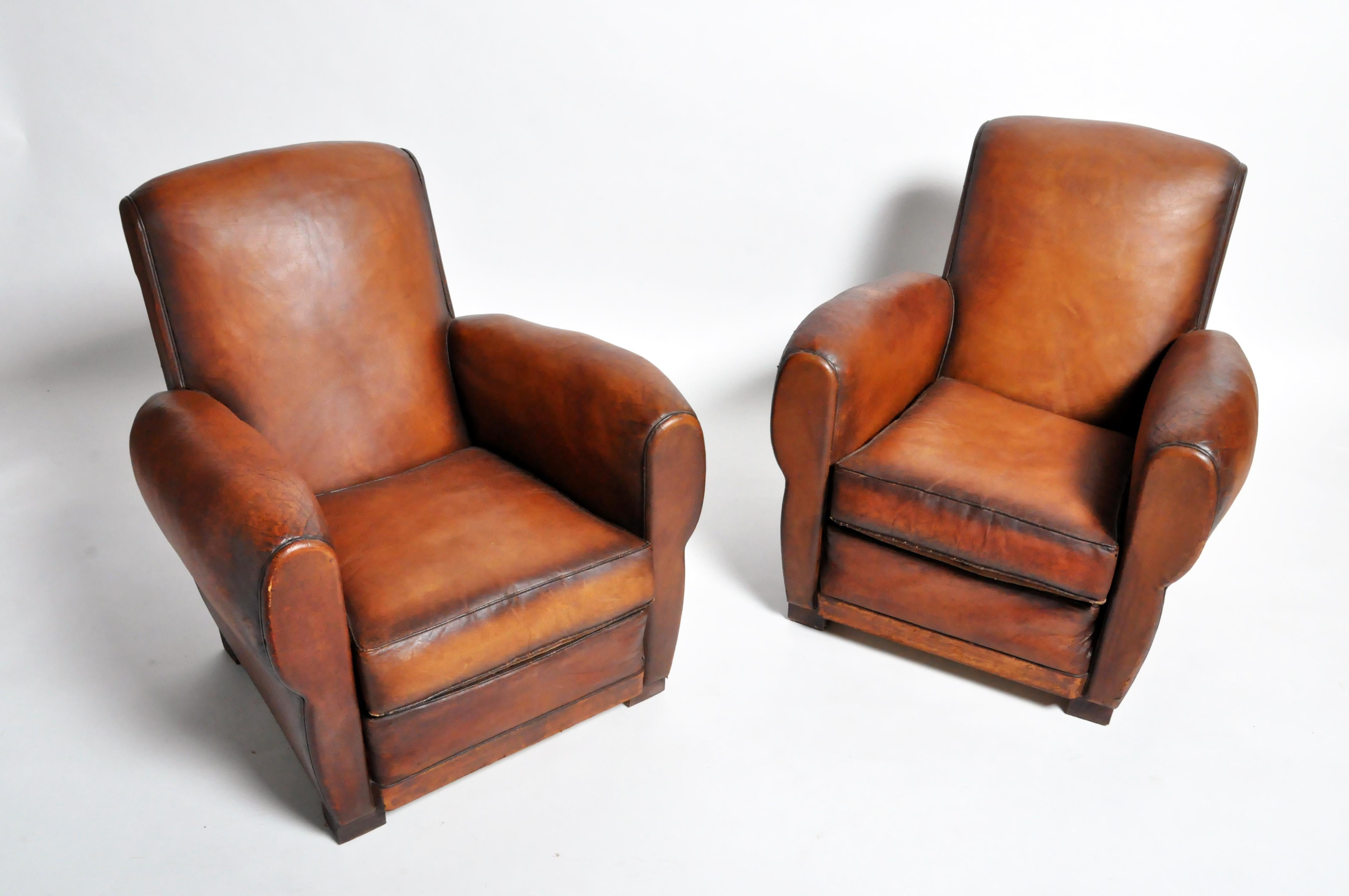 Handsome pair of club chairs from France made from leather and wood, circa 1950. Stylish and comfortable the chairs are sturdy and ready for daily use. Wear consistent with age and use.