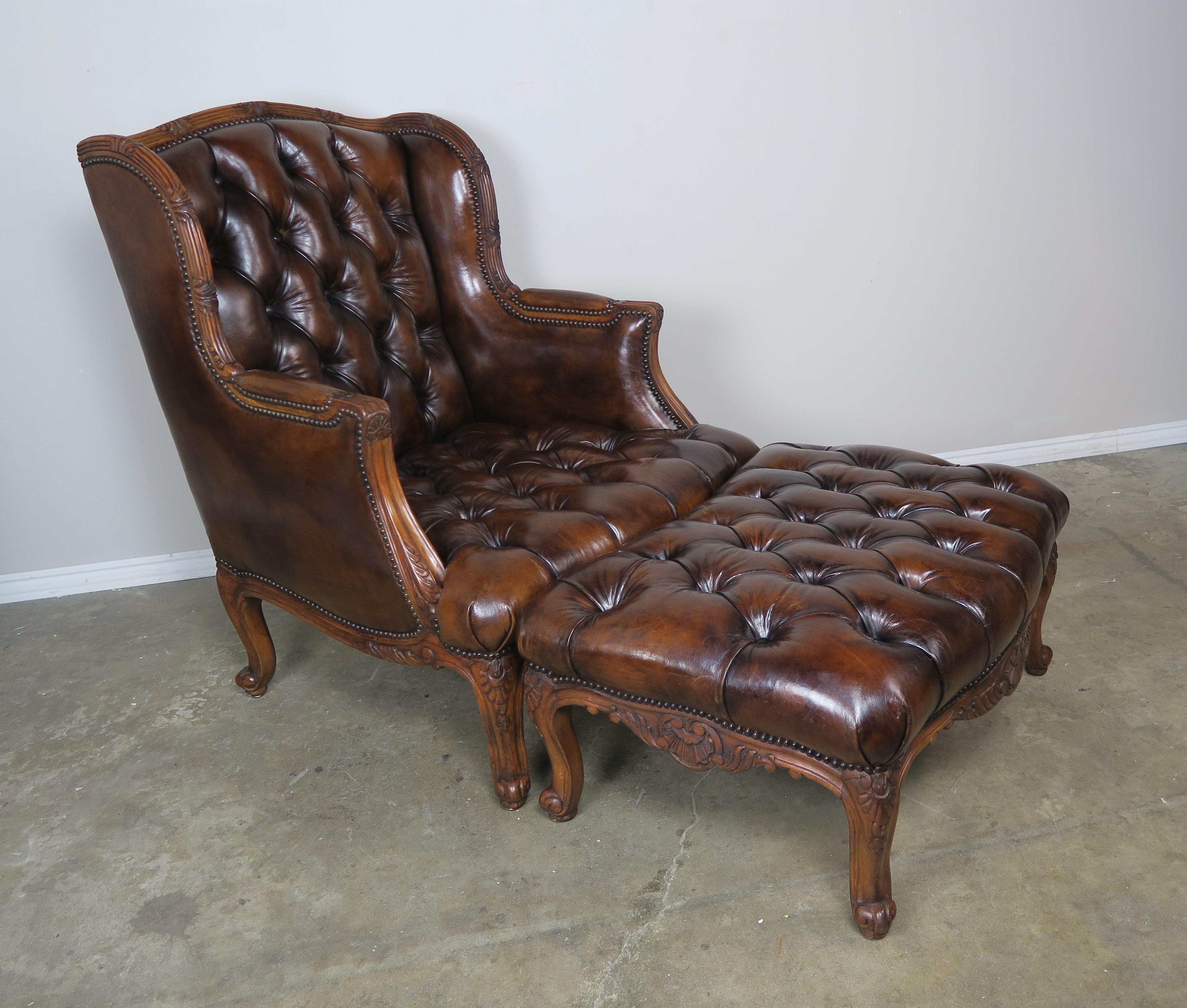 Pair of French leather wingback tufted Louis XV style chairs and ottomans that are upholstered in rich brown tufted leather with nailhead trim detail. The wingback armchairs stand on four cabriole legs as does the ottomans that end in ram's head
