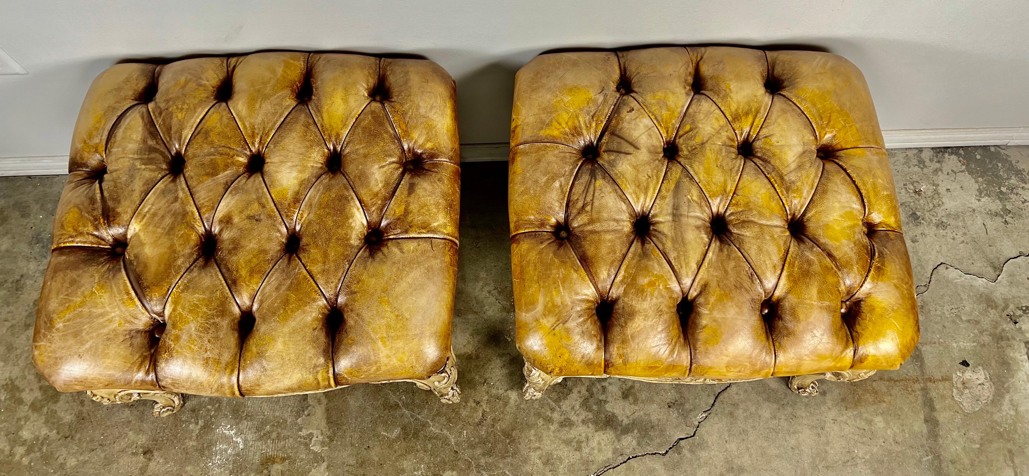 Pair of leather tufted French Louis XV style benches.  There are beautiful carved details throughout.  The bench stands on four cabriole legs that end in rams head feet.  They are upholstered in leather that has some wear but no tears or damage.  It