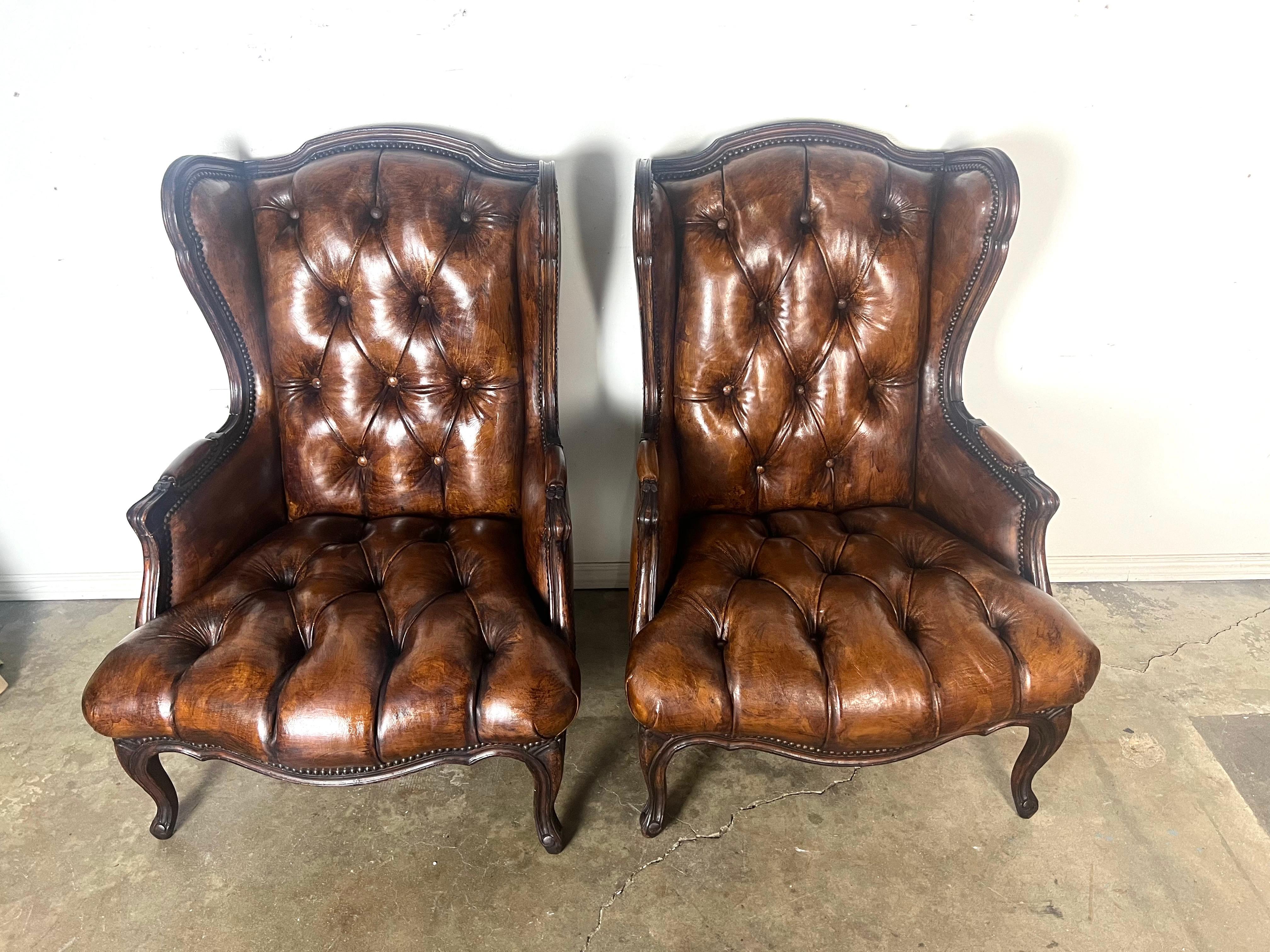 Paire de fauteuils à oreilles en cuir touffeté. Les chaises sont revêtues d'un cuir richement touffeté de couleur marron avec des garnitures en tête de clou.  Les accoudoirs sont légèrement incurvés et rembourrés, assortis au design général en cuir.