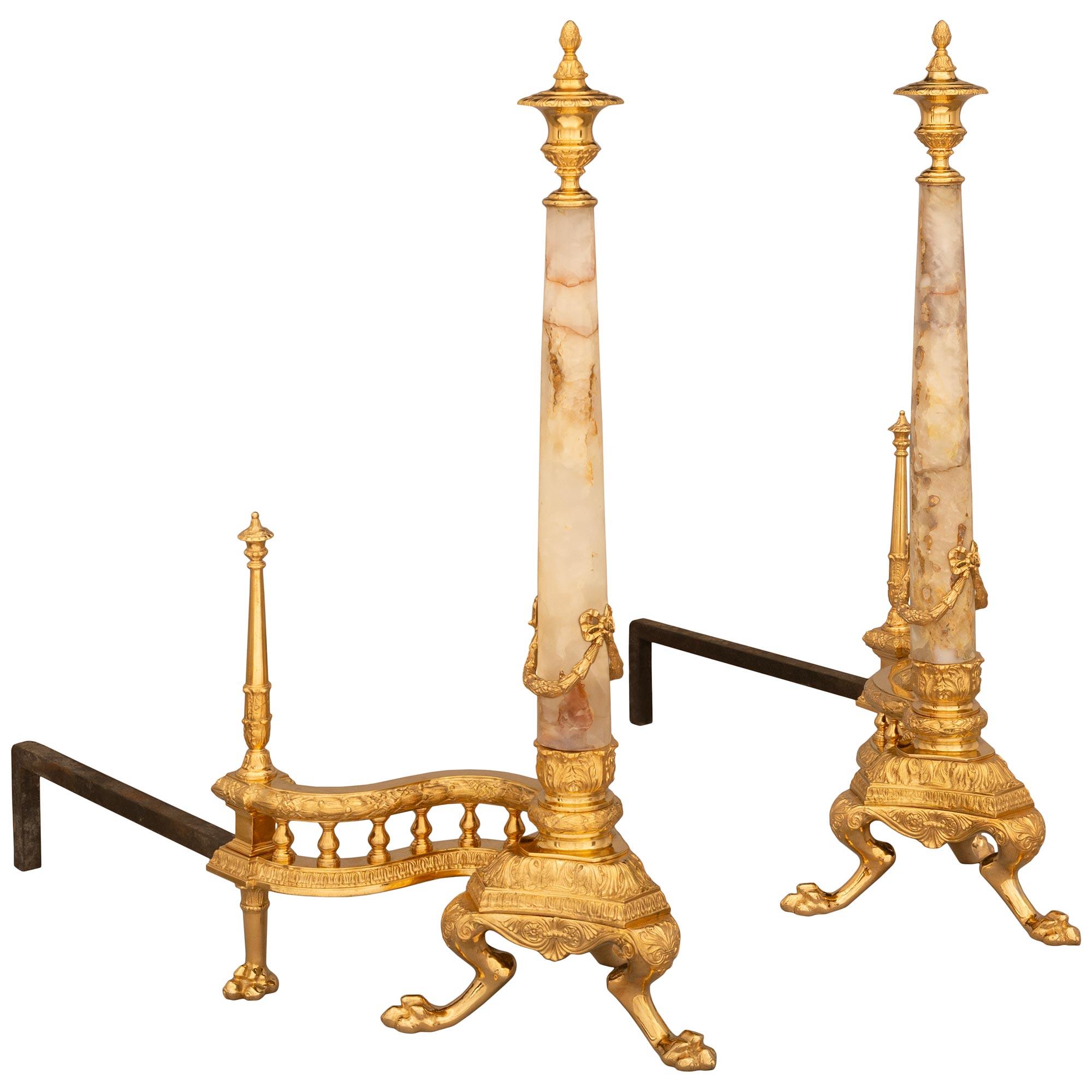 A handsome pair of French 19th century Louis Philippe period Ormolu, Onyx and Wrought Iron andirons. The pair are raised on tripod shaped bases with three pawed supports decorated by palmettes. The supports flank a scalloped shaped apron below the