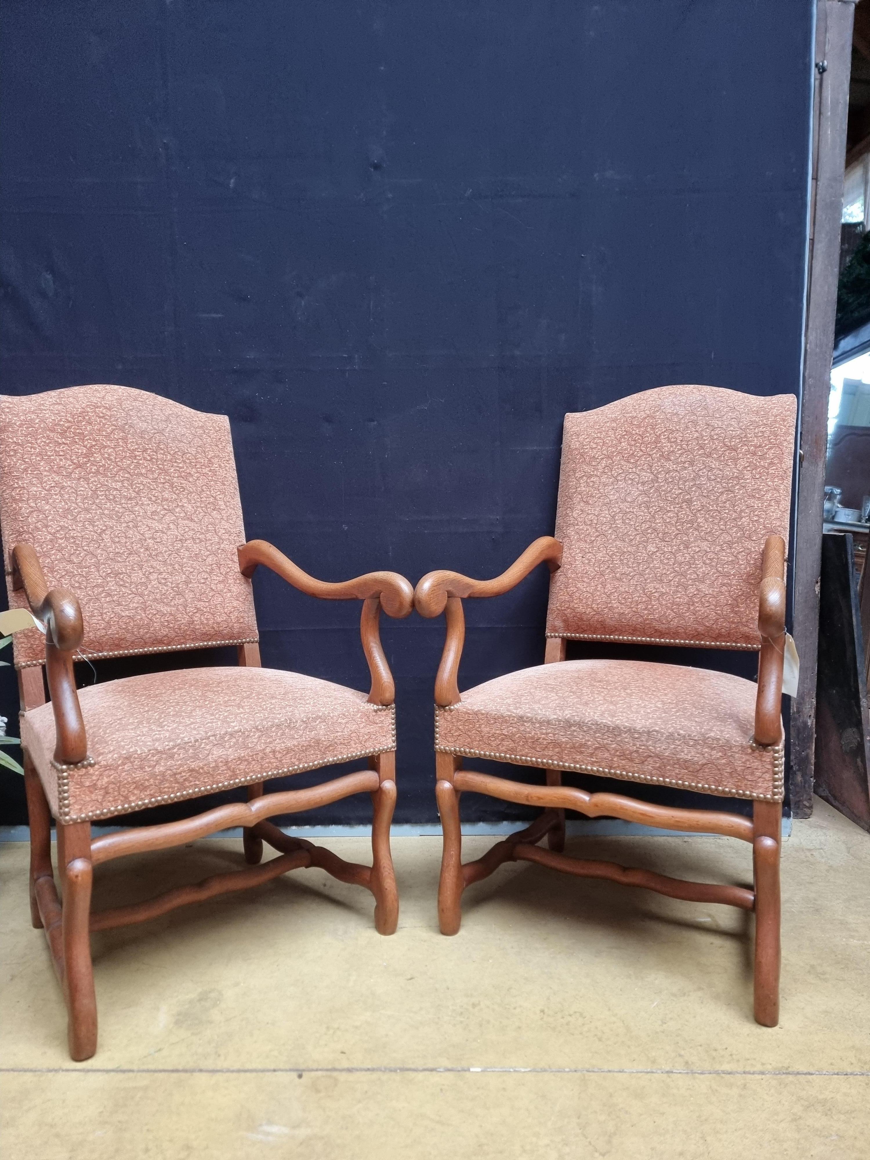 A pair of French Louis XIII style walnut os de mouton legs armchairs from the 20th century with large scrolling arms. Discover the timeless elegance and robust charm of these French Louis XIII style walnut armchairs, a pair that gracefully combines