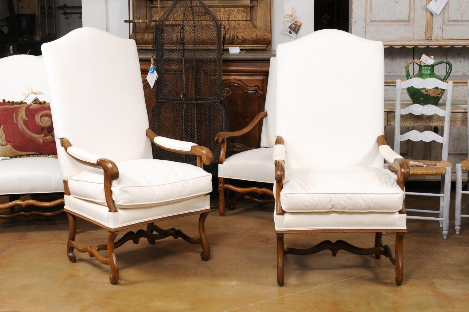 A pair of French Louis XIV style walnut fauteuils from the 19th century, with scrolling legs, cross stretchers and new upholstery. Created in France during the 19th century, each of this pair of armchairs features a slightly slanted camelback