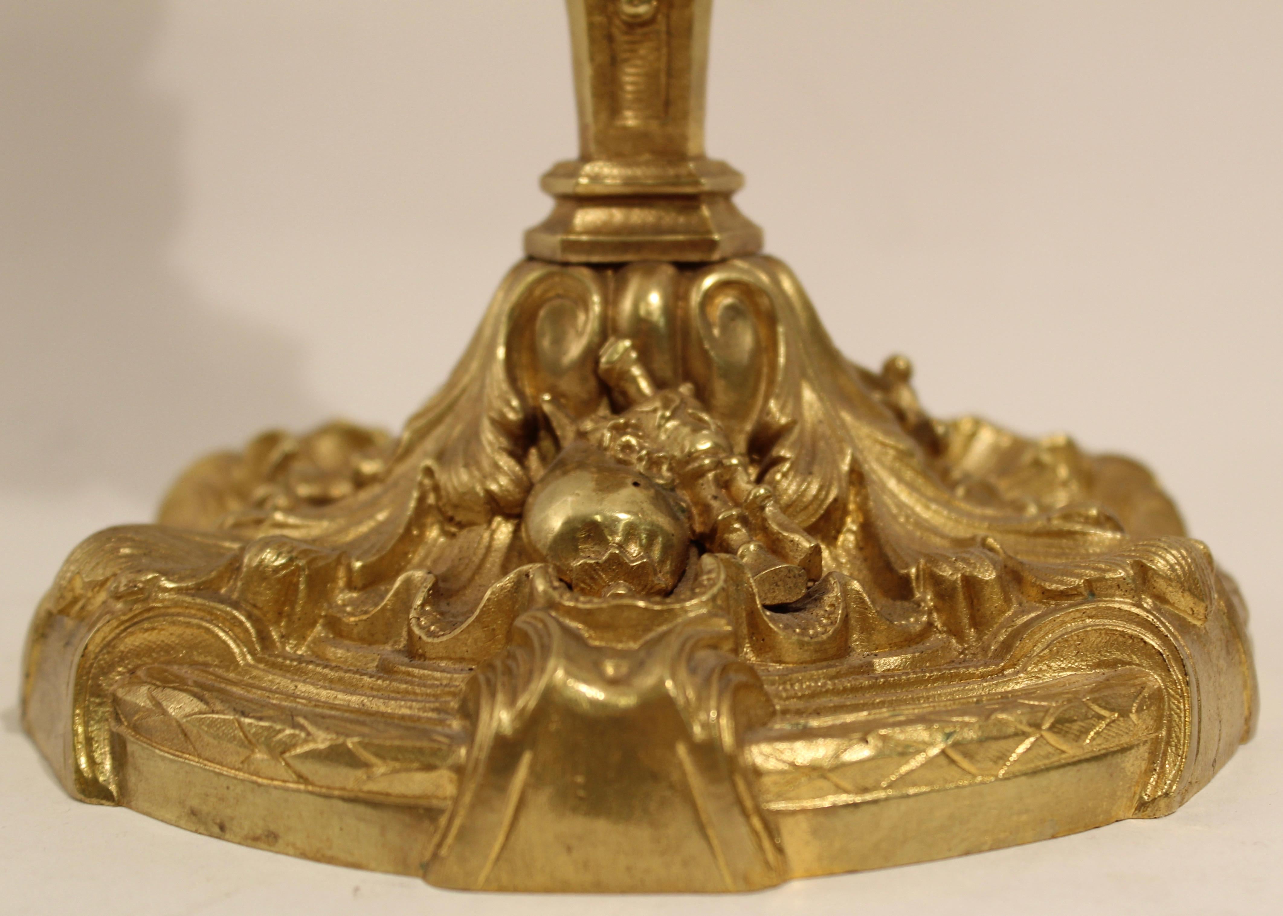Pair of French Louis XIV style candlesticks, circa 1850. The circular foliate ormolu base decorated with instruments, below a triform column with faces of court jesters and fauns, above this, an urn shaped candleholder.
 