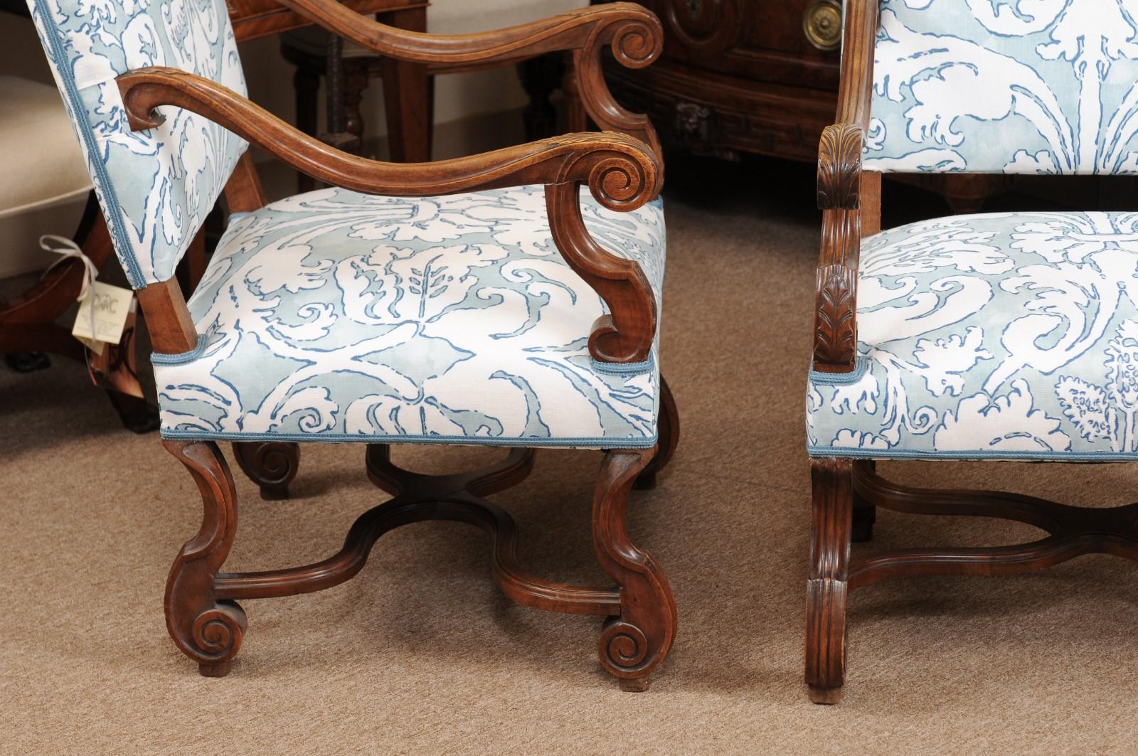 The pair of French Louis XIV style walnut armchairs/ fauteuils in pale blue/ off-white linen upholstery with high rectangular backs, carved down slept scrolled arms and carved mutton bone legs joined by X-stretcher.