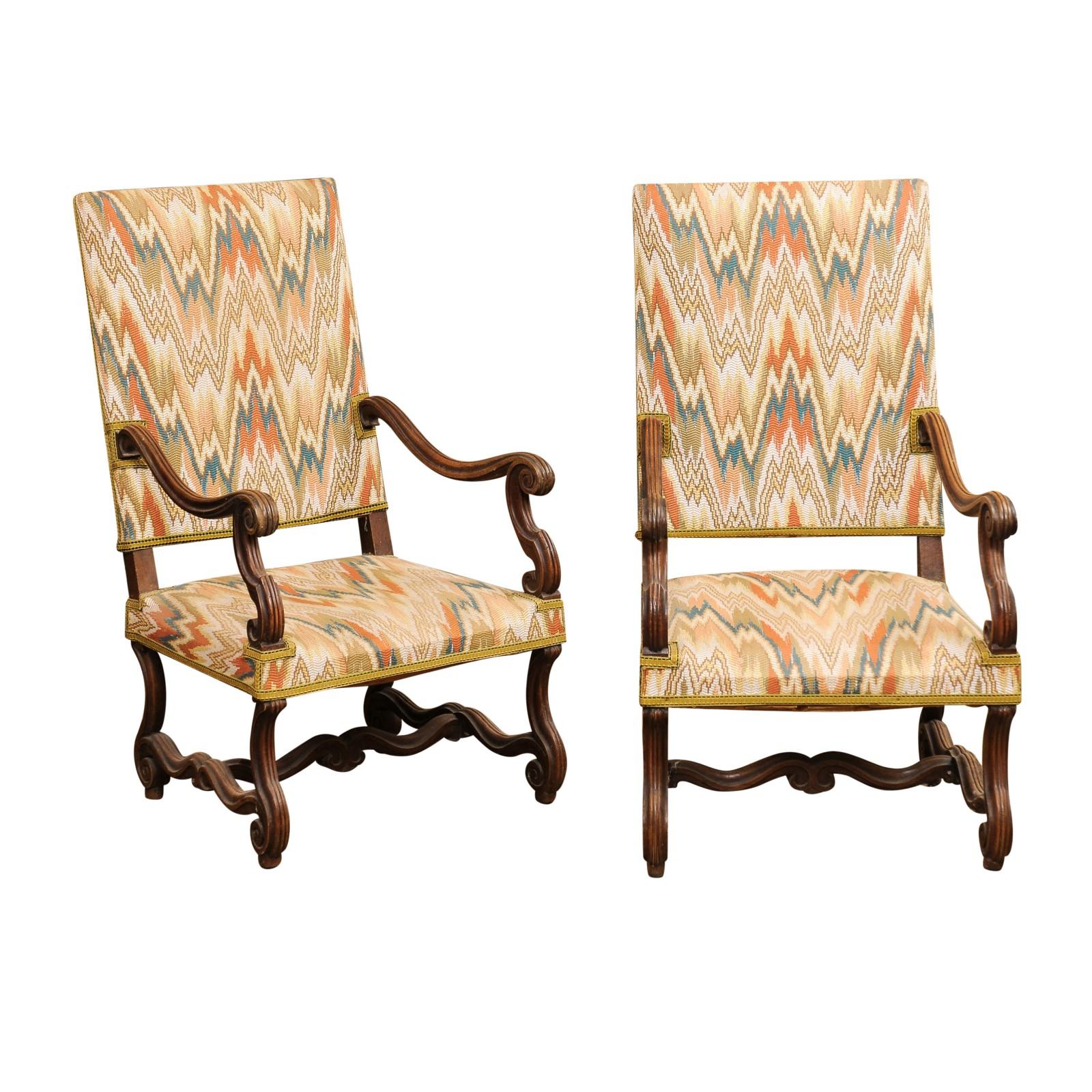 A pair of French Louis XIV style walnut os de mouton fauteuils from the 19th century with rectangular slanted backs, large scrolling arms, scrolling legs, cross stretchers and flame stitch upholstery. Presenting this pair of 19th-century French