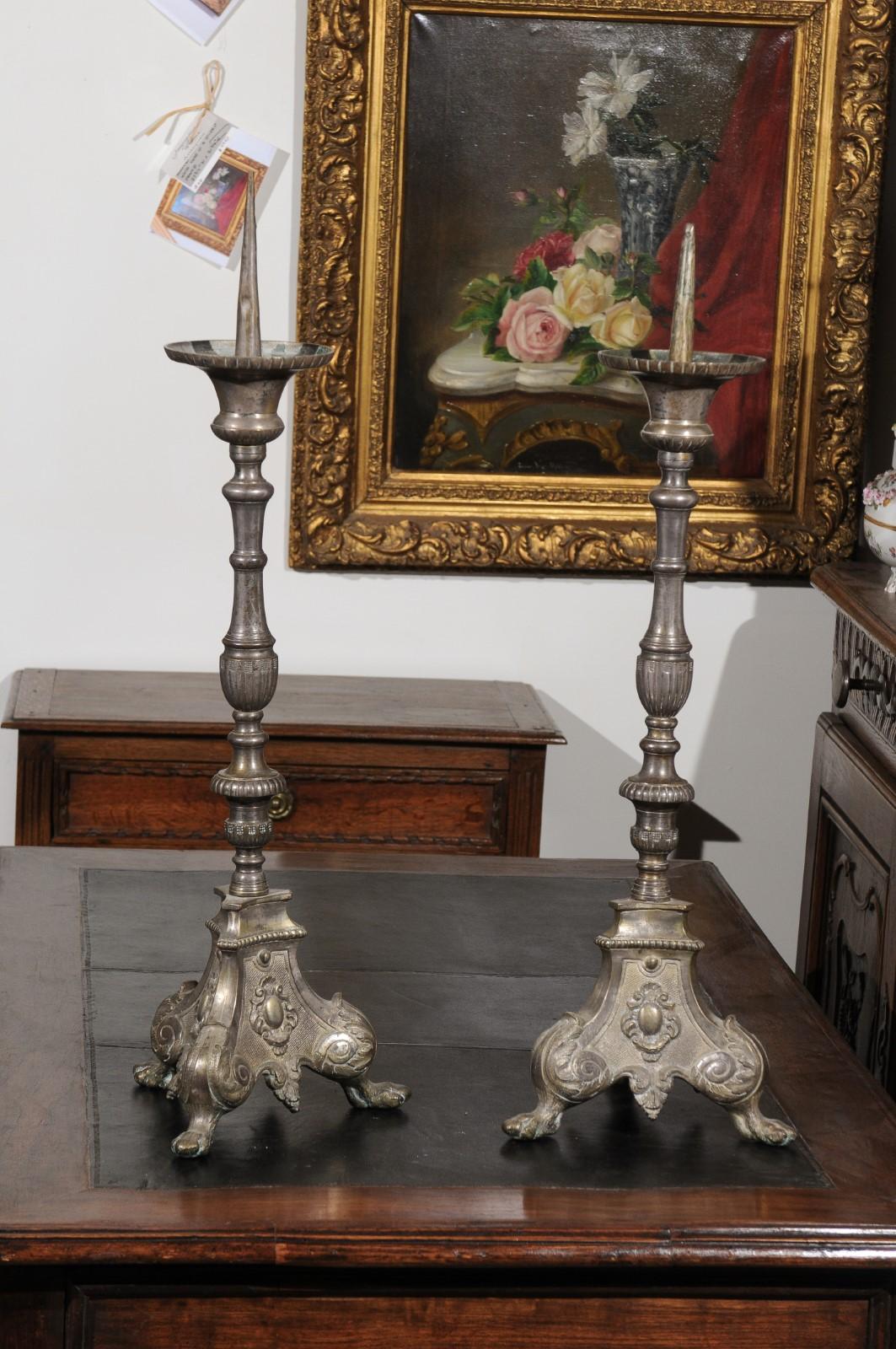 A pair of French Louis XV silvered bronze candlesticks from the 18th century, with volutes and paw feet. Born in France during the reign of King Louis XV nicknamed the Beloved, each of this pair of exquisite silvered bronze candlesticks features a