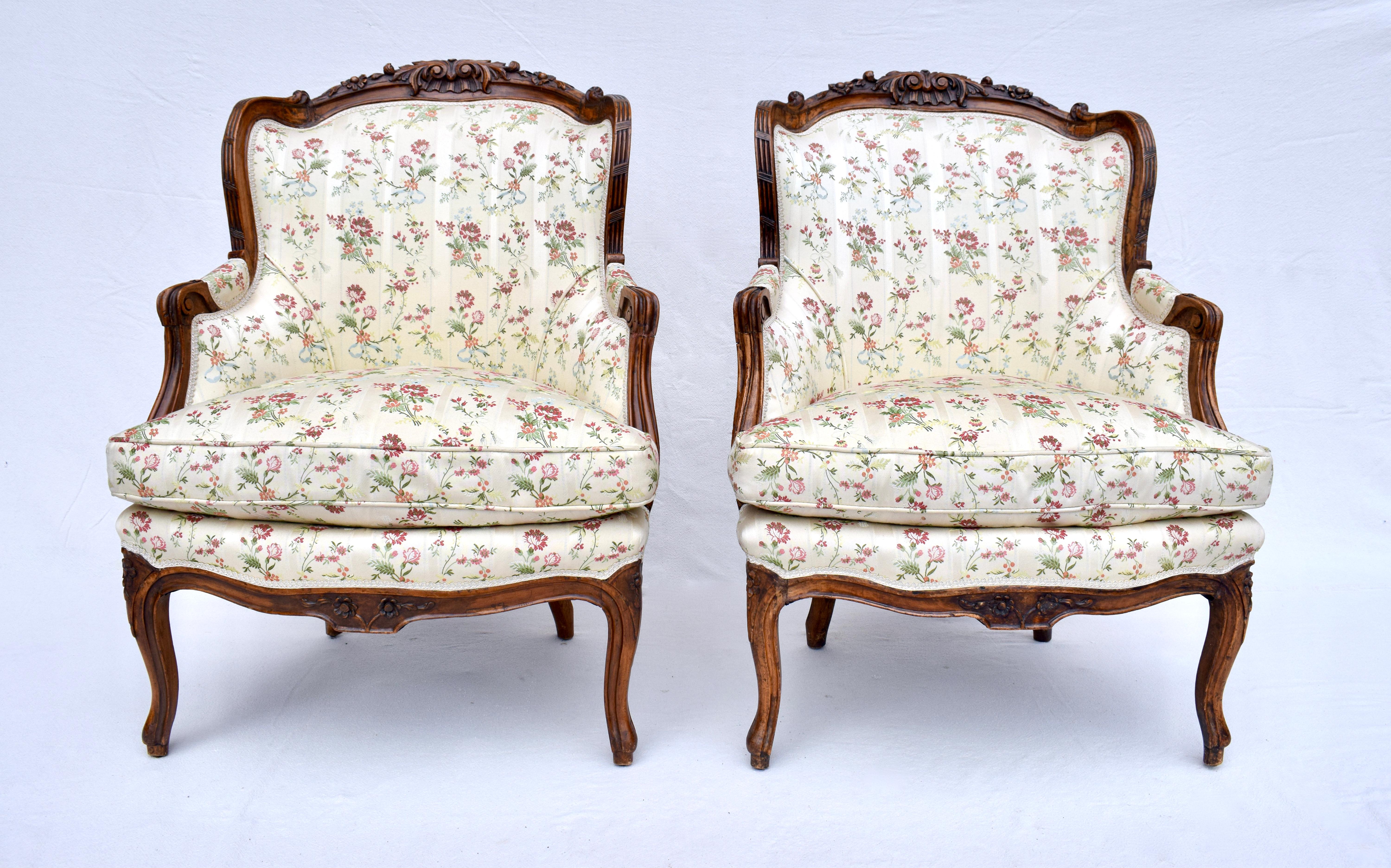 A pair of Intricately hand carved mid 19th C. French Bergere chairs upholstered in floral silk with plump goose down loose cushions. Seat Height: 21