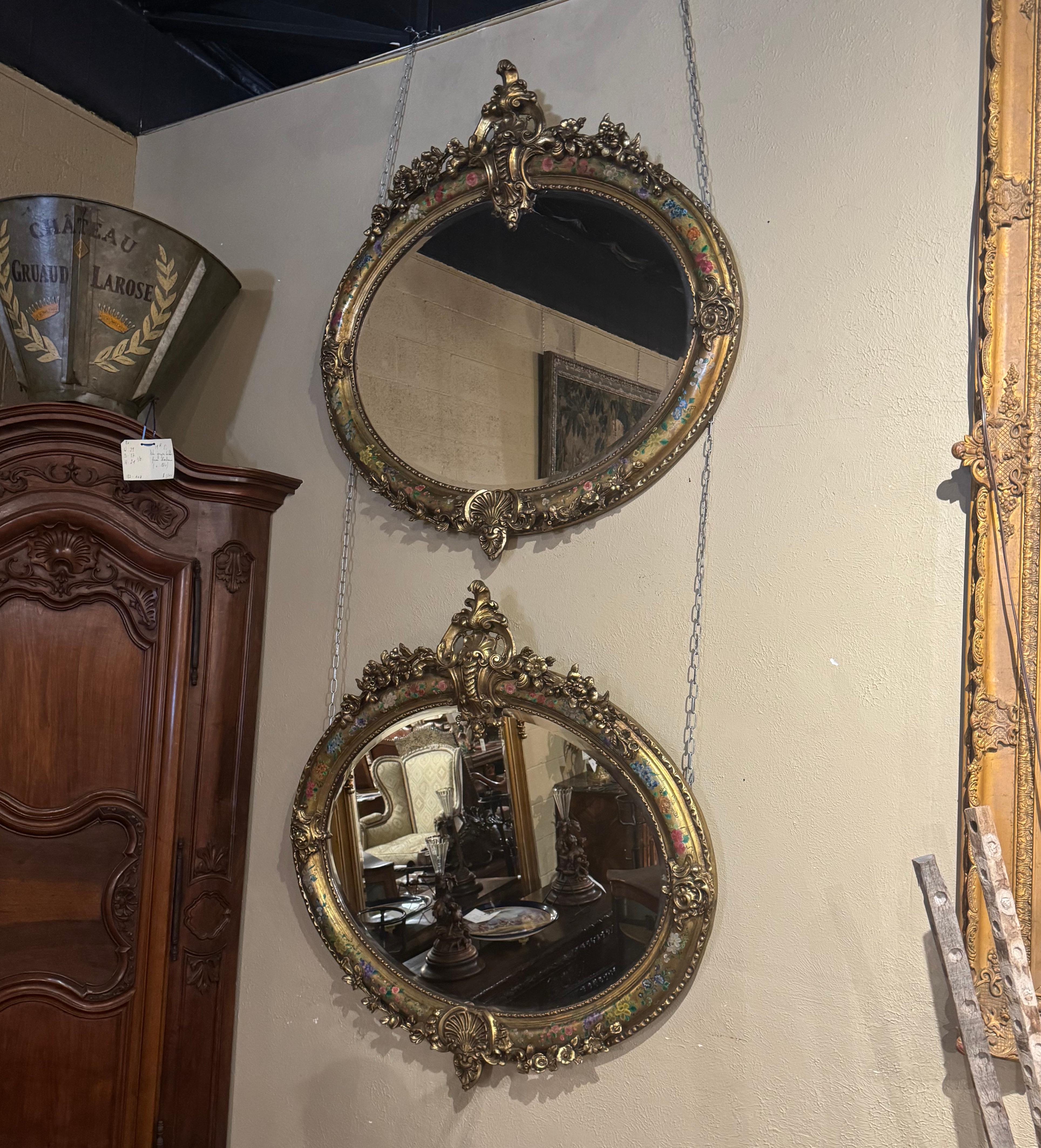 Décorez une salle de bains principale avec cette paire de miroirs muraux assortis. Chaque cadre ovale est caractérisé par un travail élaboré de rinceaux dorés, y compris un cartouche rocaille ajouré au fronton, un décor de feuillage à la base, tous