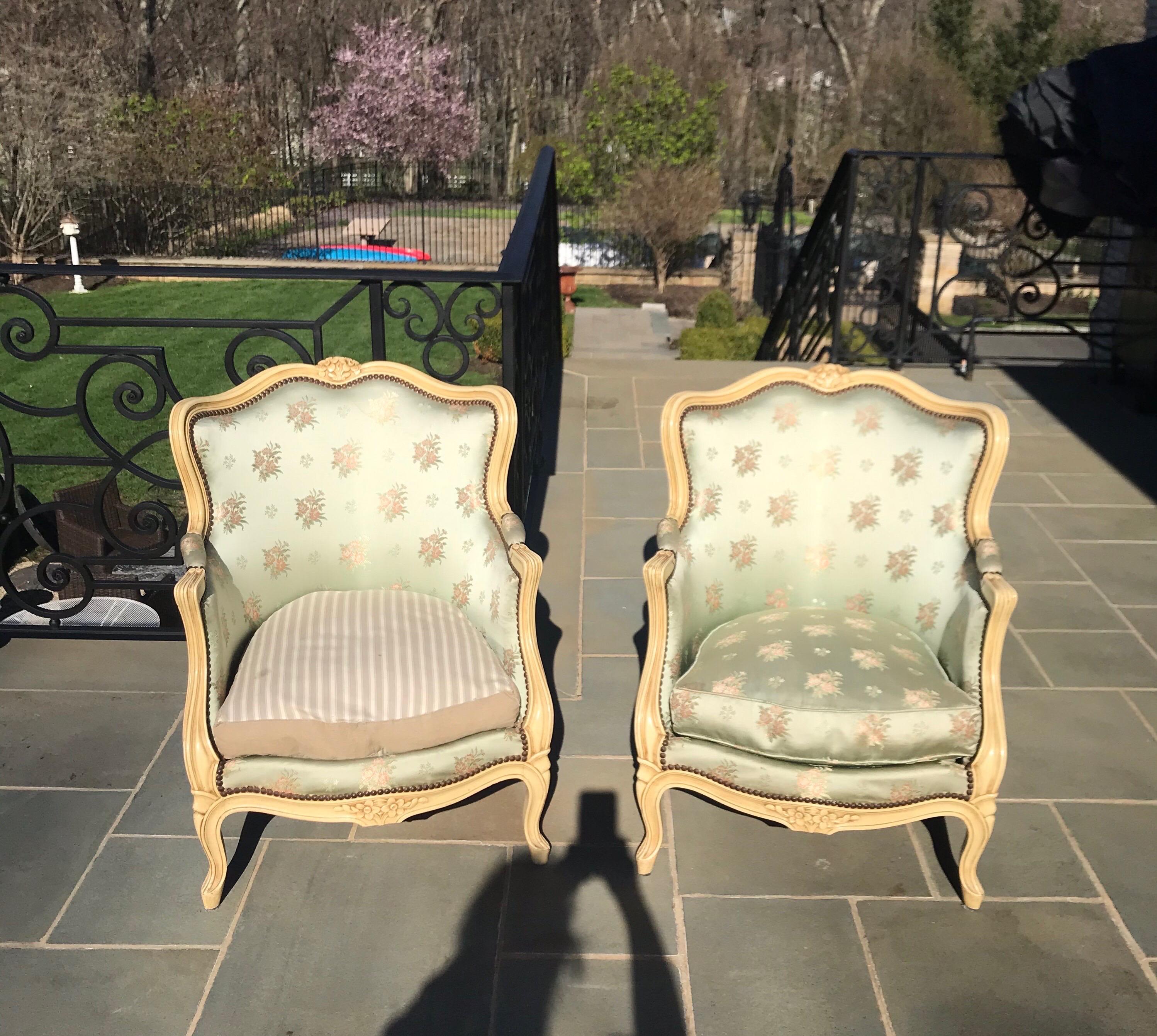 The French Louis XV style ivory painted bergere chairs has sweeping lines and beautifully carved flowers. The original silk brocade fabric can be reupholstered to add elegance to any room decor.