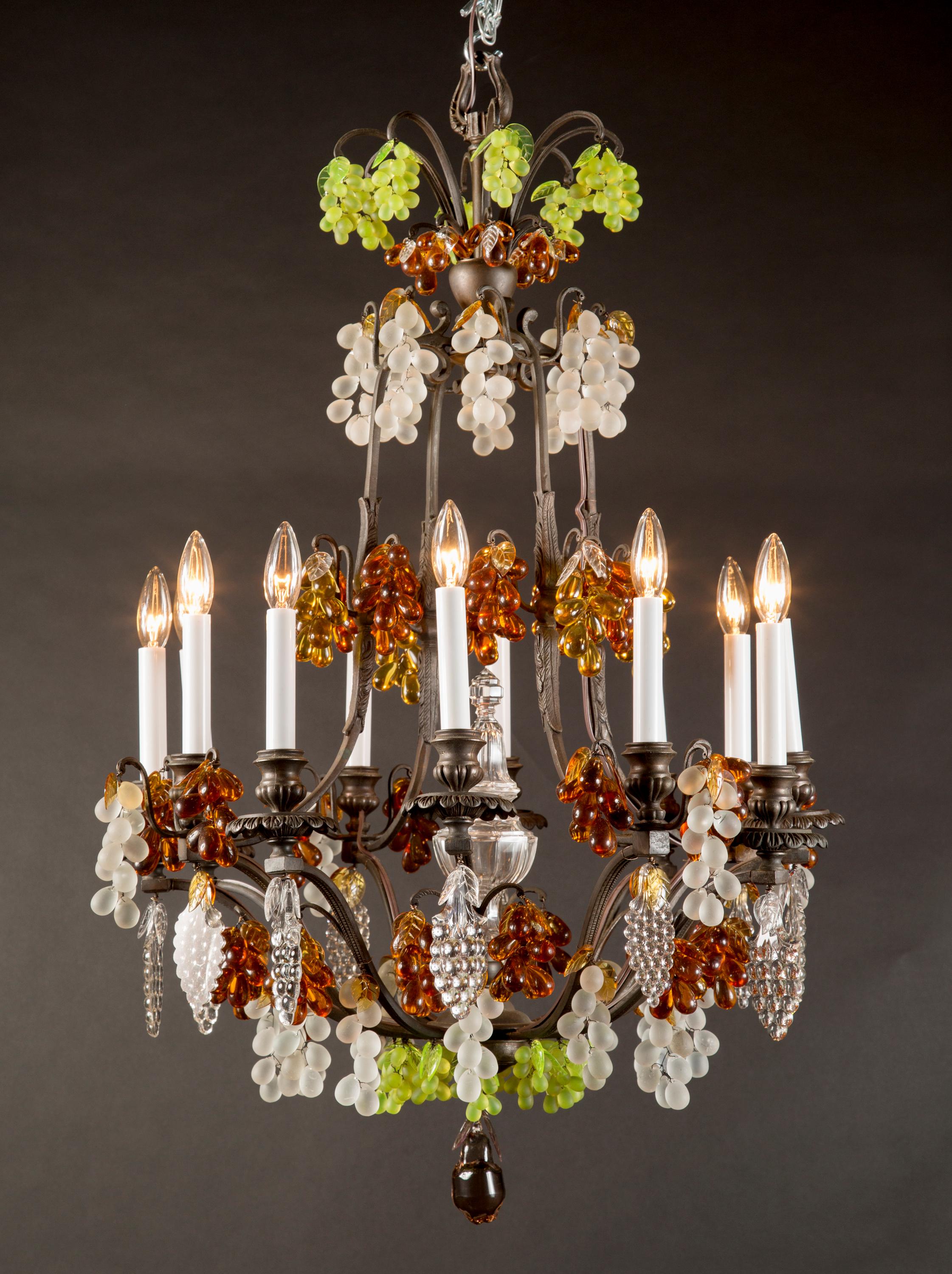 This beautiful pair of French patinated bronze chandeliers feature the bird cage shape Classic to the Louis XV style. The pair is draped with bunches of colored crystal grapes and adorned with finely etched crystal leaves. A large clear crystal