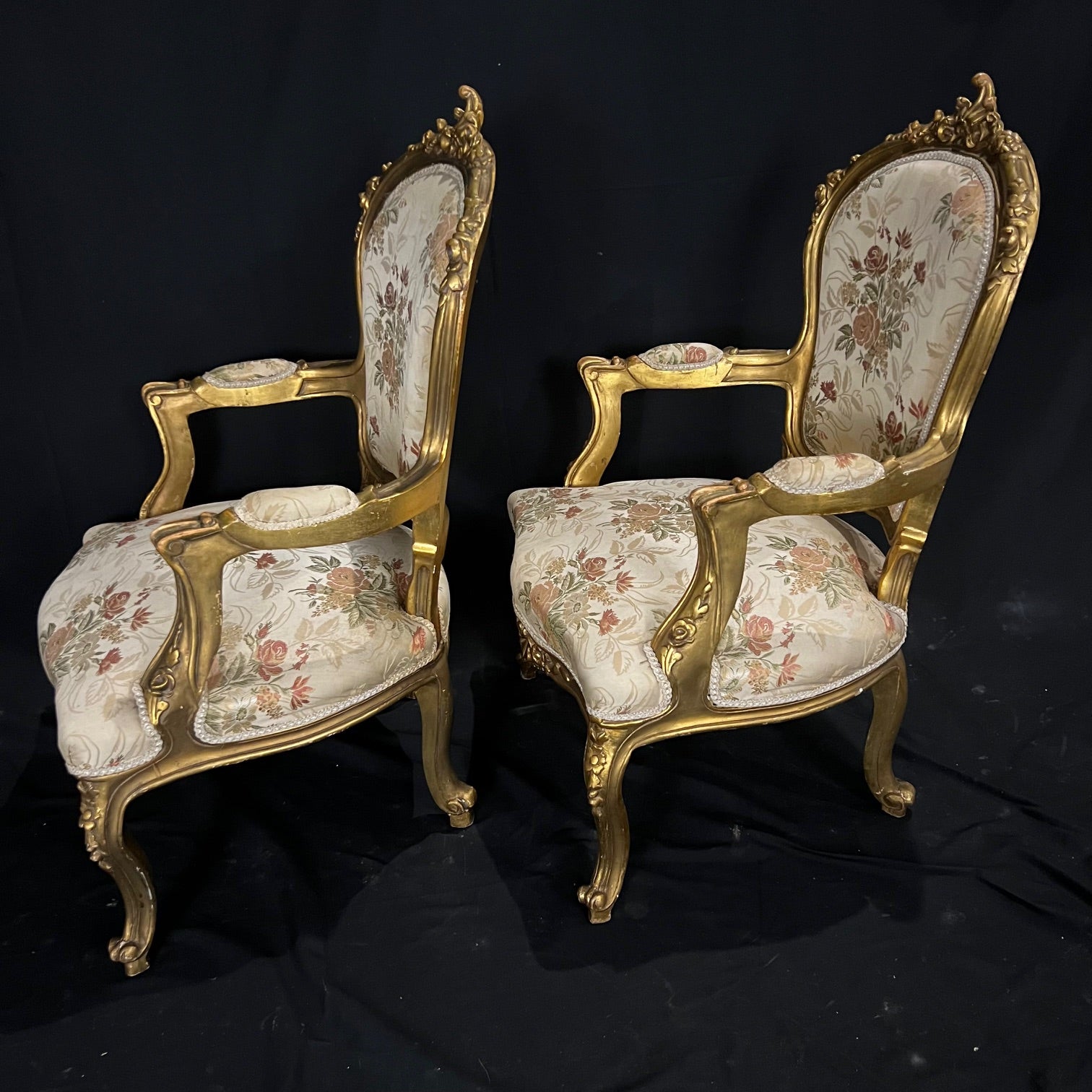 Deux fauteuils ouverts en bois doré de style Louis XV, chacun avec un dossier en cartouche, surmonté d'une sculpture florale, des accoudoirs en volutes et des sièges en forme reposant sur des pieds cabriole. Tapissé d'un tissu floral polychrome. #