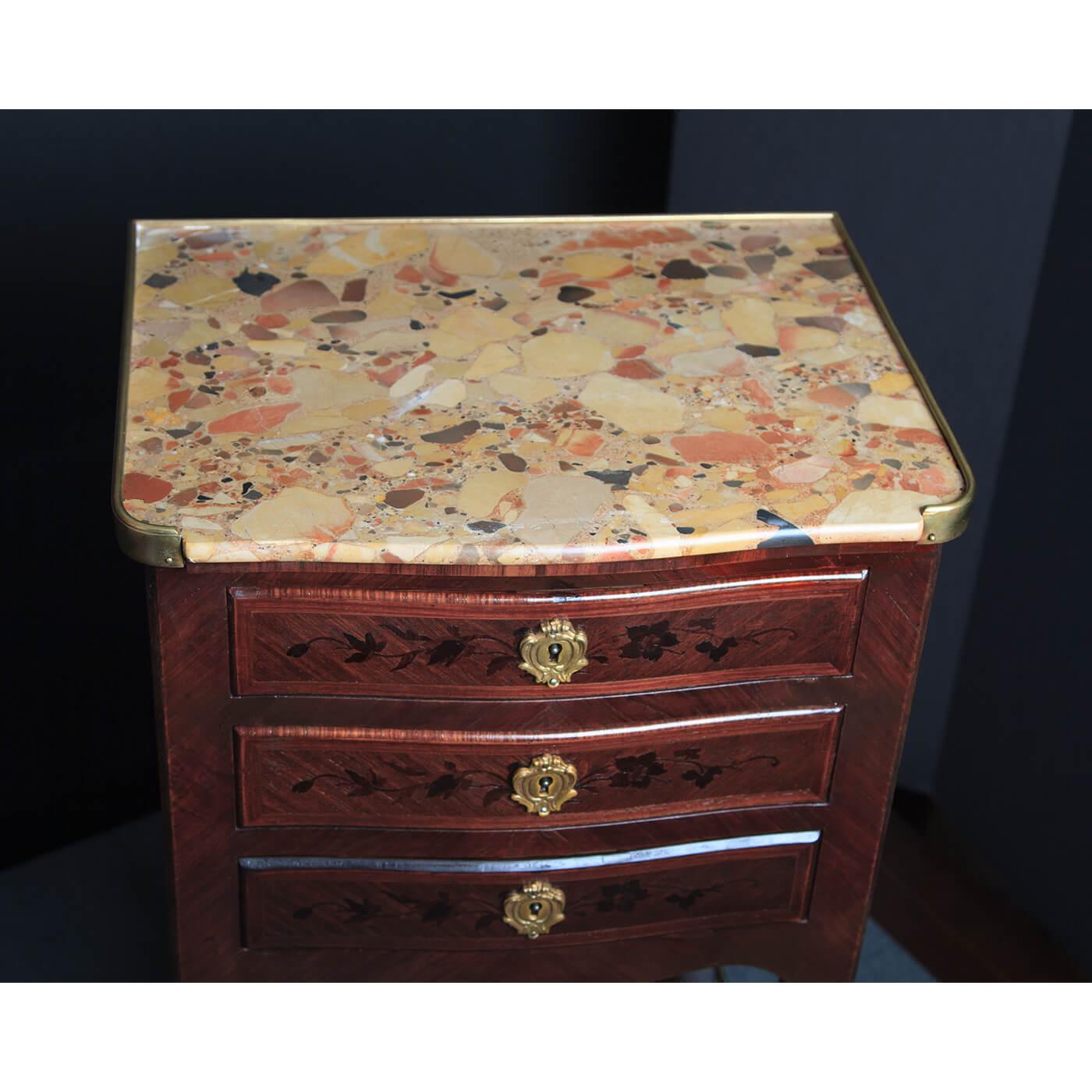 A pair of French Louis SV marble top marquetry inlaid petit commodes. The pair with a Breche D'Alep marble top, a brass gallery, above three floral marquetry inlaid drawers with Rococo bronze mounts, with shelf stretchers and bronze sabots. France,