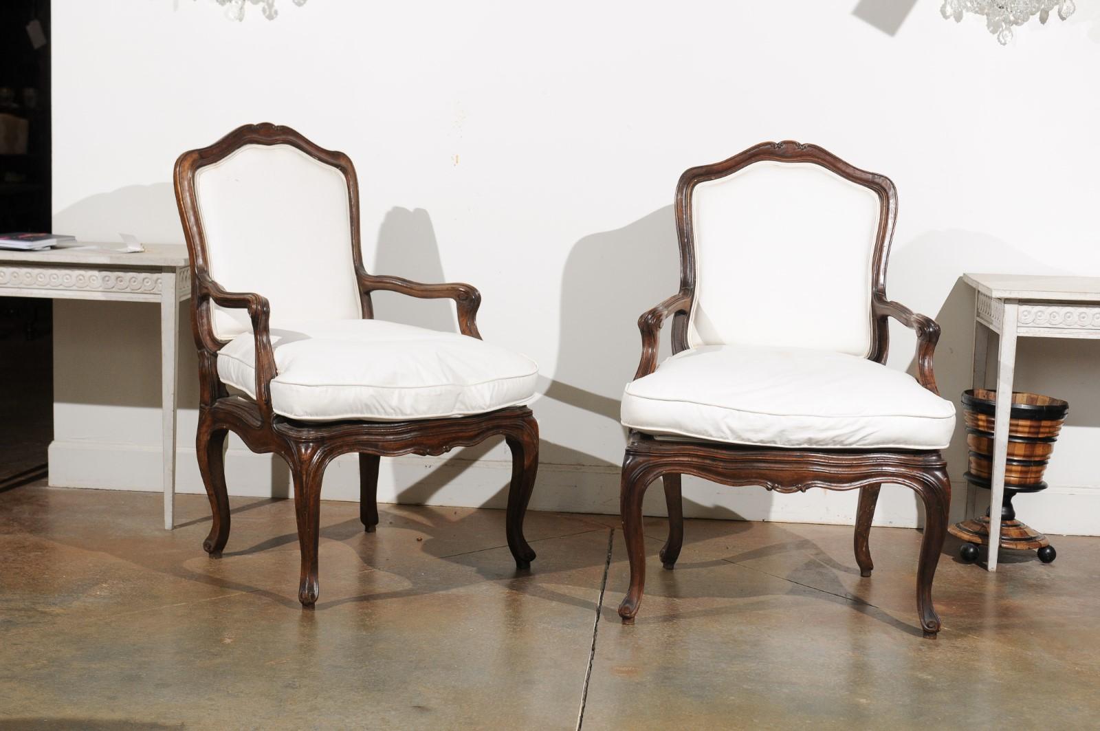 A pair of French Louis XV style walnut fauteuils from the early 19th century, with double welt upholstery and cabriole legs. Born in France during the Restauration period, each of this pair of armchairs features a slightly slanted back topped with a