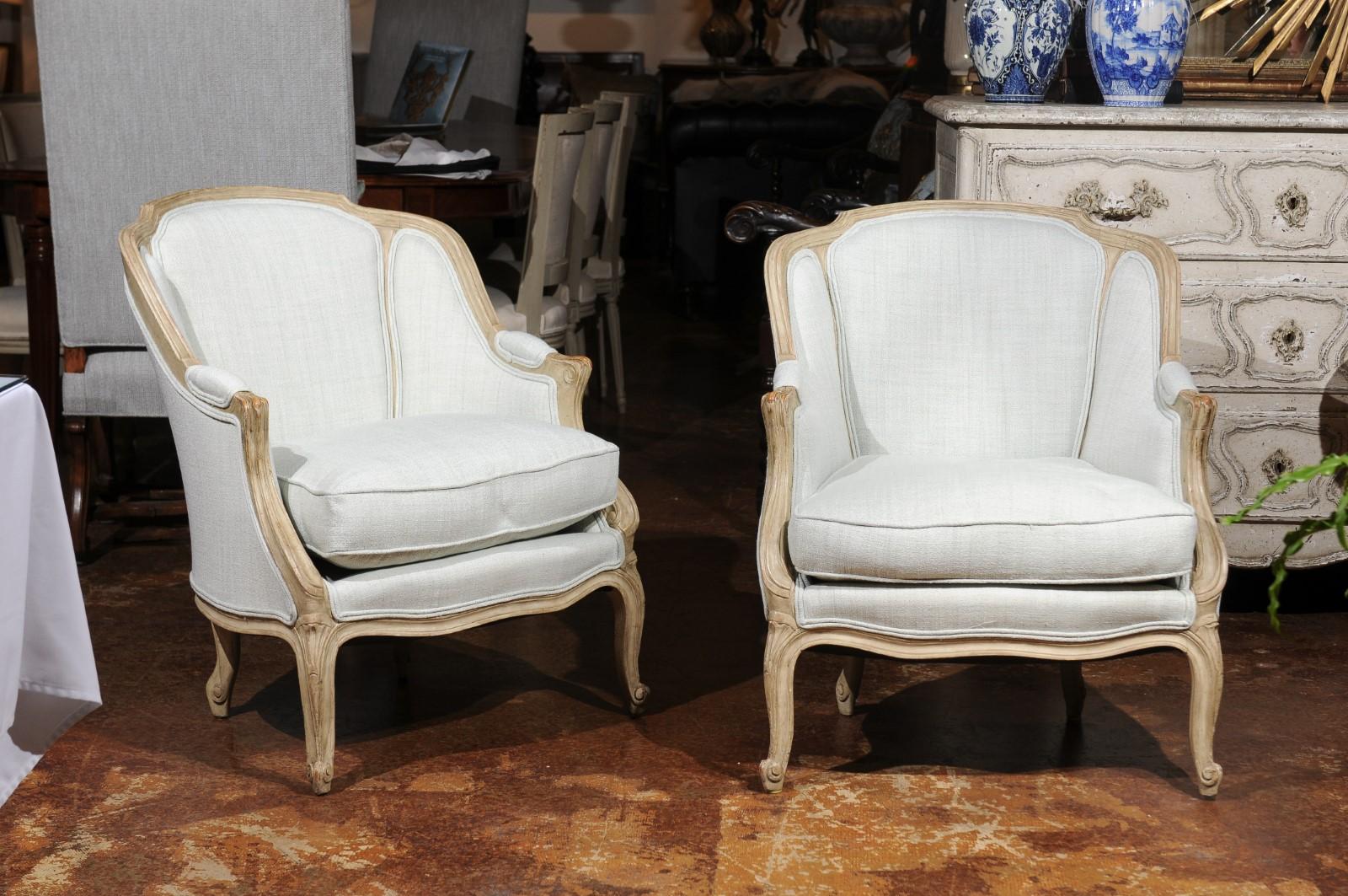 A pair of French Louis XV style painted bergères armchairs from the late 19th century with wraparound backs, cabriole legs and new upholstery. Born in the later years of the 19th century, each of this pair of French bergères features an enveloping