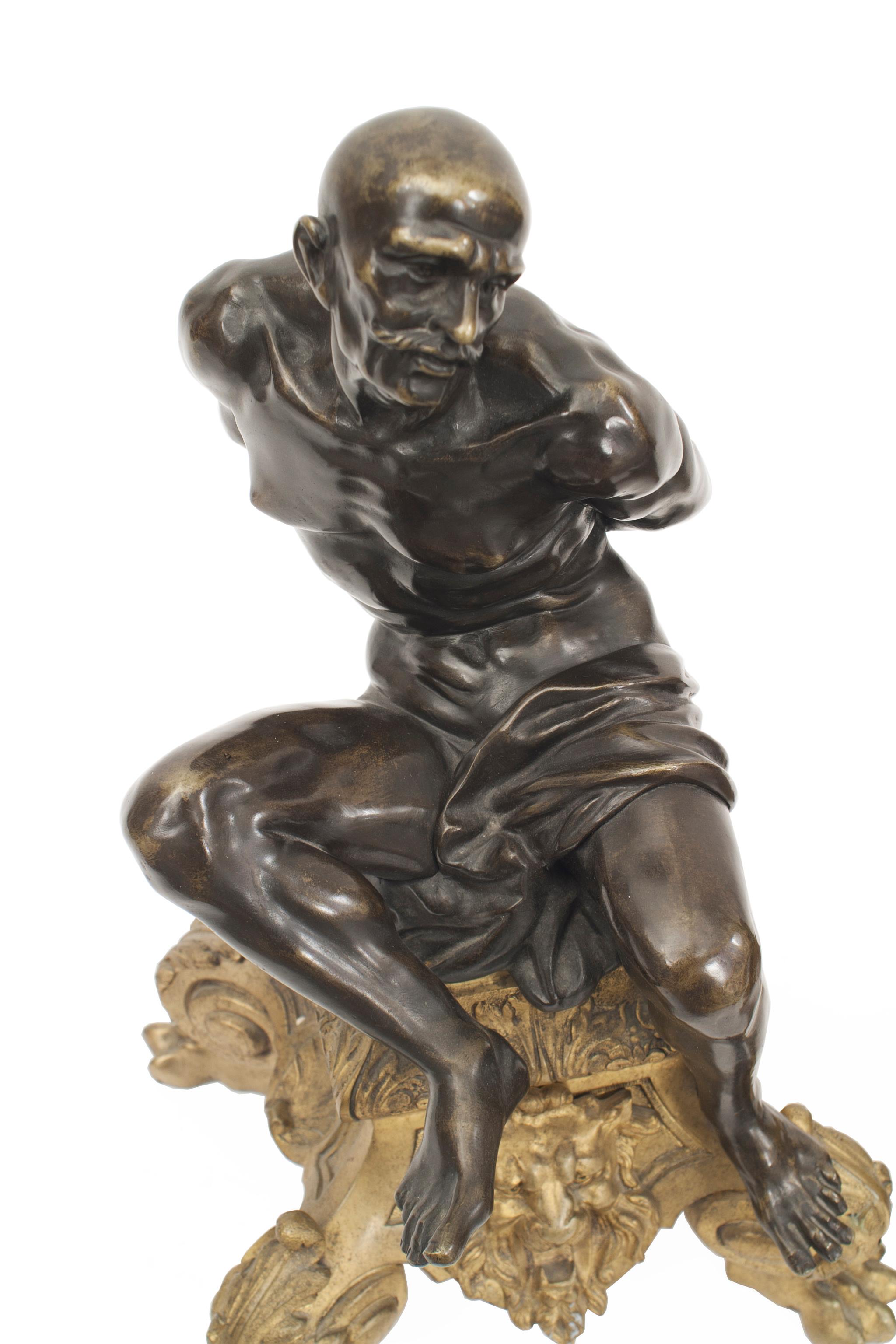 Paire de chenets en bronze de style Louis XV (19e siècle) représentant deux figures masculines ligotées sur une base dorée.
 