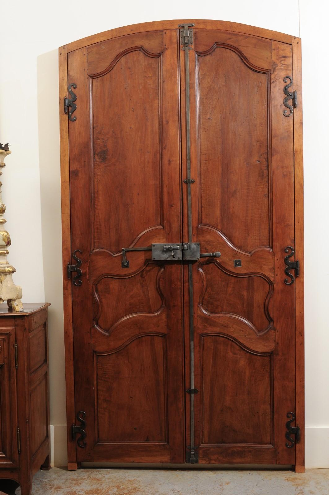 A pair of large scale French 19th century Louis XV style doors in alder wood, with custom-made door surrounds. We currently have a pair of doors available. This pair of French doors features an arched top, sitting above a pair of double doors,