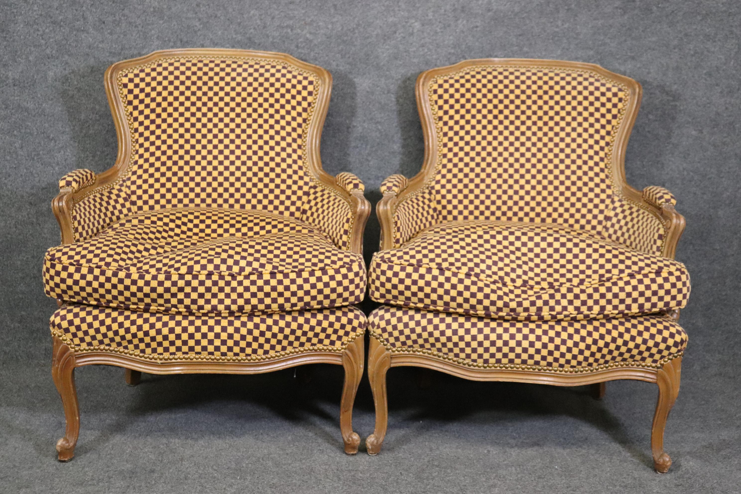 This is a beautiful pair of French Louis XV style bergeres. They are upholstered in vintage yellow and lavender upholstery with a checkerboard pattern. The chairs date to the 1960s and will show signs of wear and use. The chairs measure 39 tall x 29