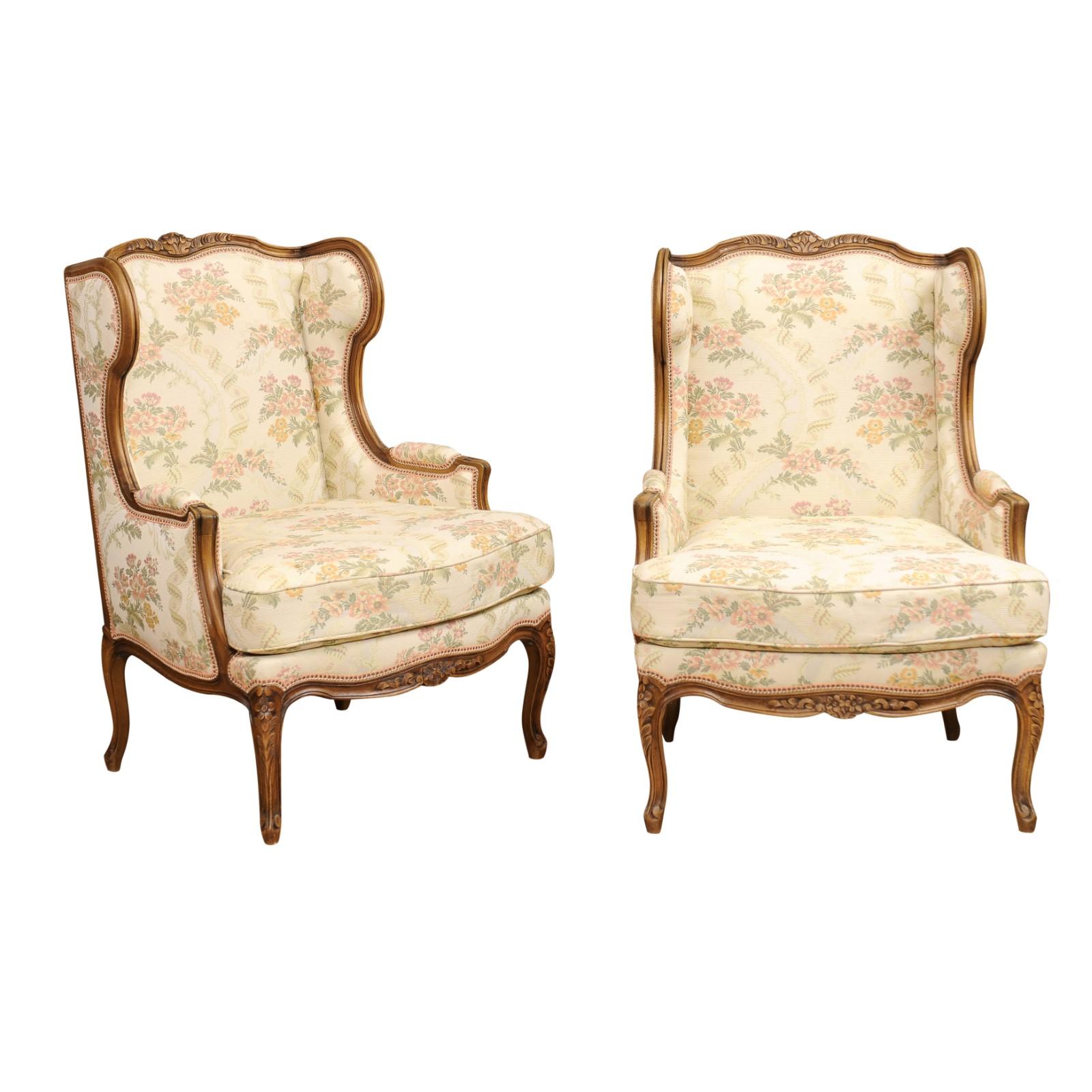 A pair of French Louis XV style walnut bergères à oreilles from the 20th century, with carved floral décor, upholstery and cabriole legs. Created in France during the 20th century, this pair of wingback bergères, called bergères à oreilles in