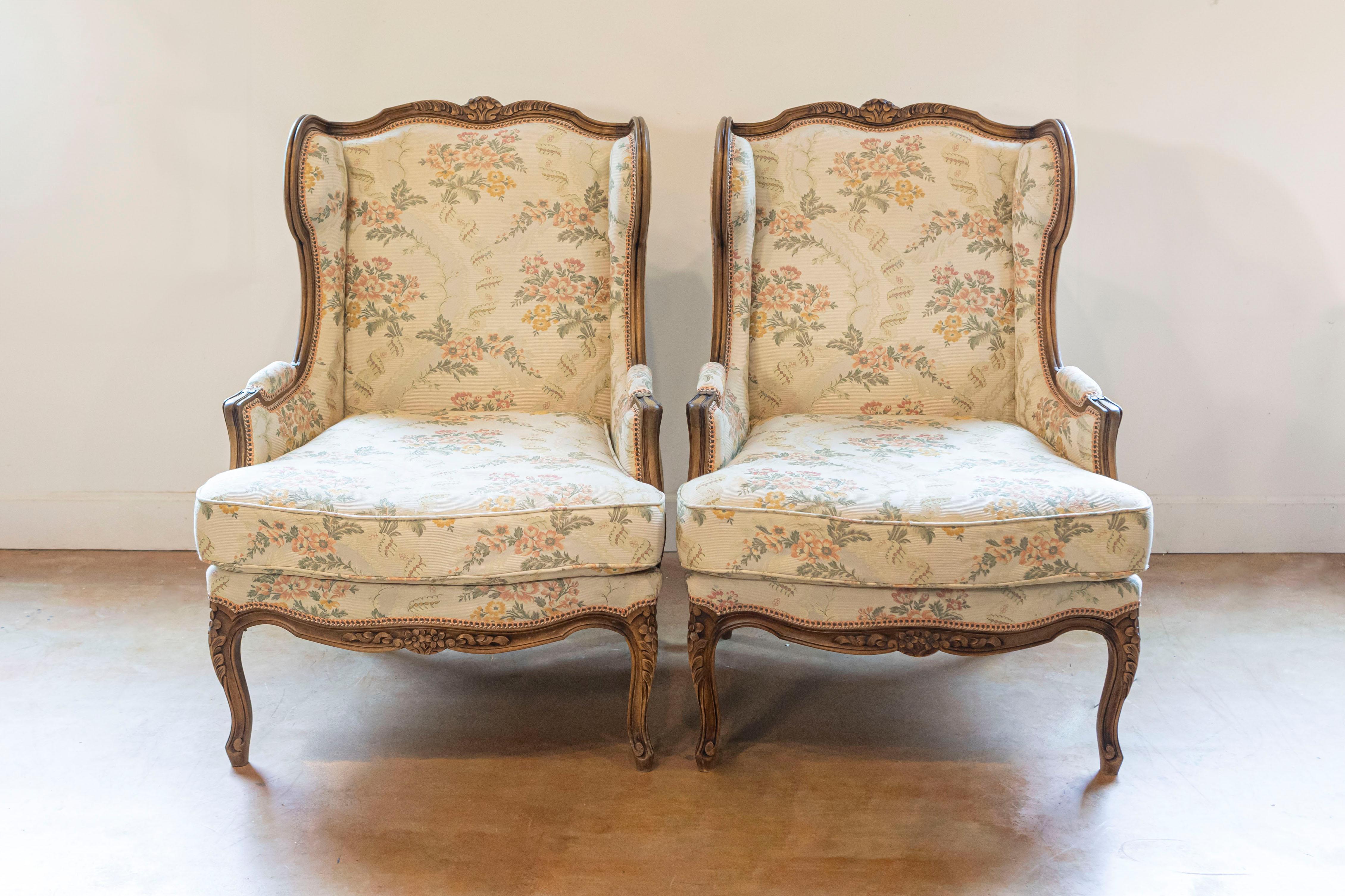 A pair of French Louis XV style walnut bergères à oreilles from the 20th century, with carved floral décor, upholstery and cabriole legs. Created in France during the 20th century, this pair of wingback bergères, called bergères à oreilles in