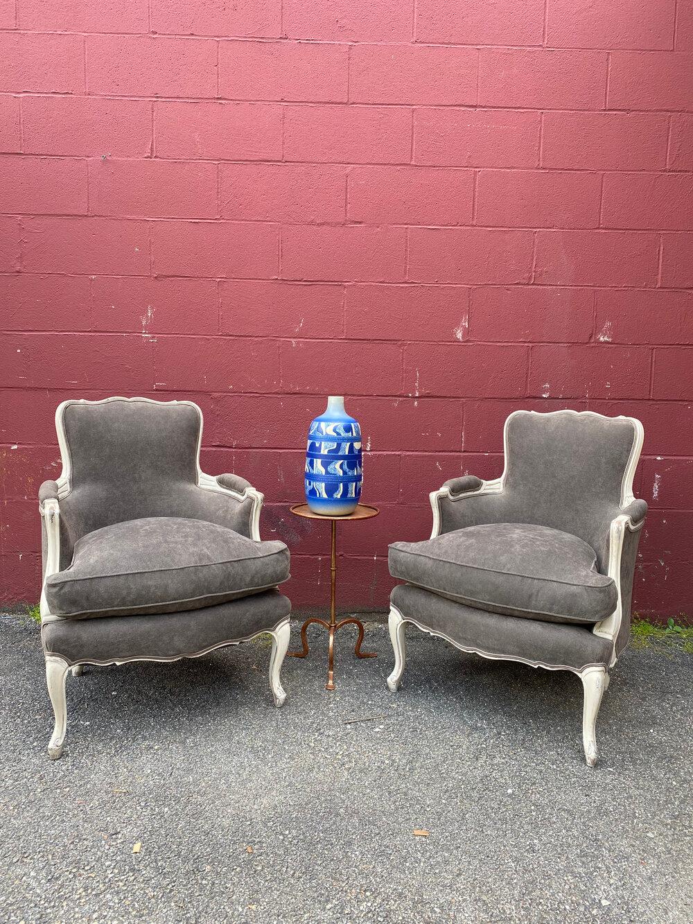 An elegant pair of French Louis XV style armchairs upholstered in gray fabric. Discover timeless beauty with this exquisite pair of Louis XV style bergeres. Timeless and luxurious, these chairs will add elegance and sophistication to any room. The