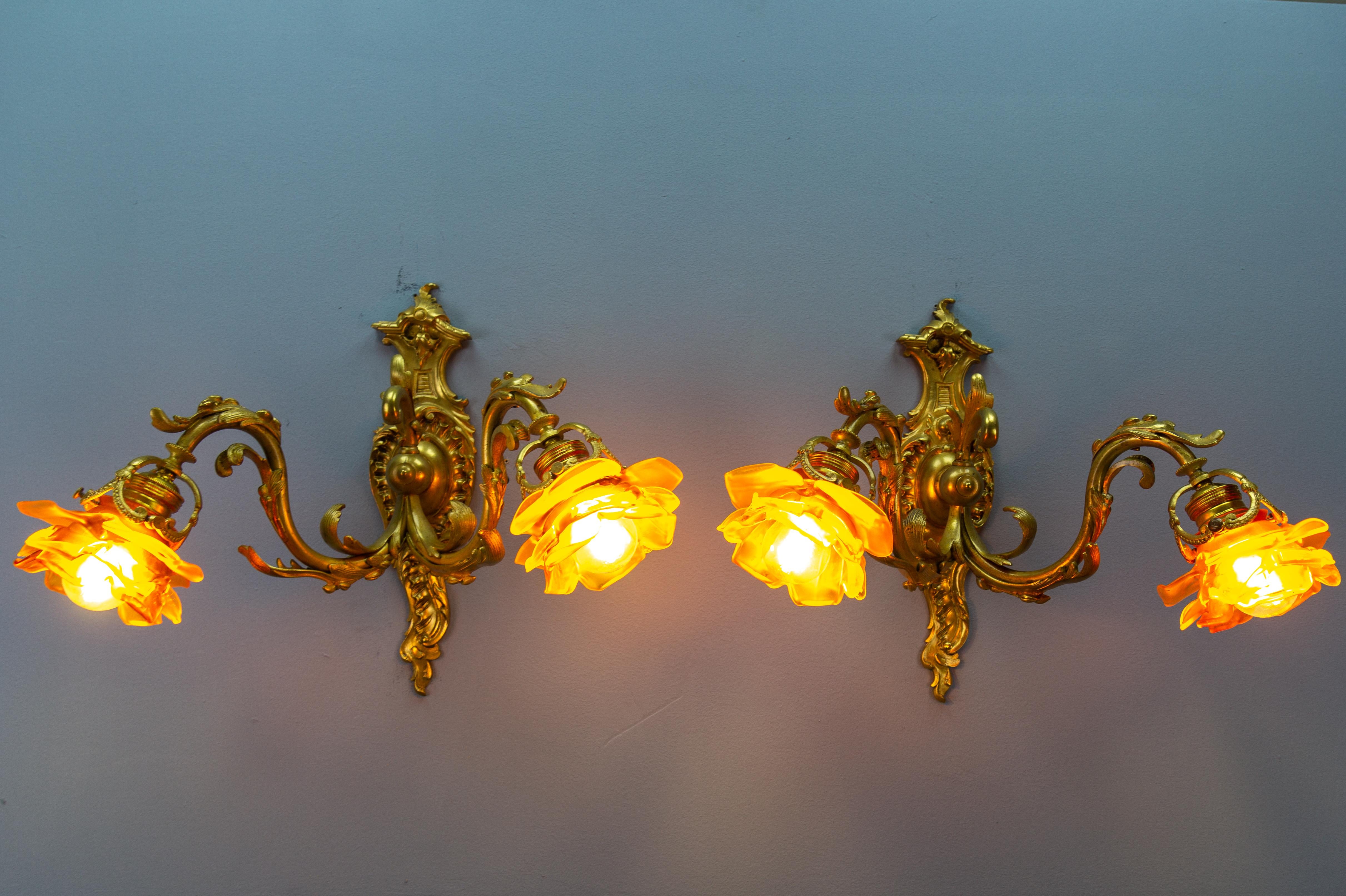 Pair of French Louis XV style bronze and brown glass twin arm sconces from ca. 1900.
These large, impressive Louis XV or Rococo-style sconces feature bronze arms and a backplate of characteristic Rococo design, of scroll shape with scrolling foliate
