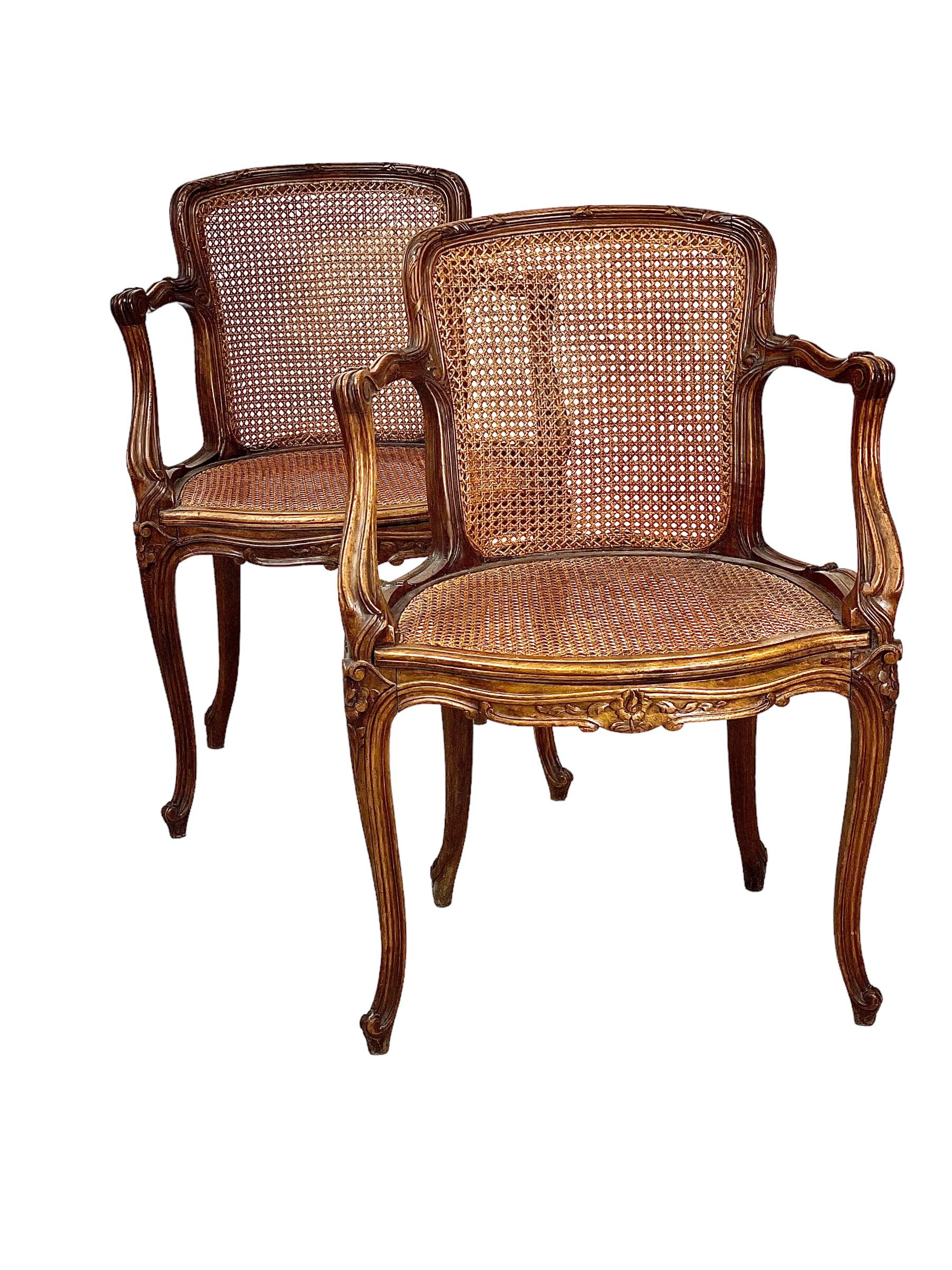 An exceptionally comfortable pair of French Louis XV style ‘Fauteuils Cabriolets’ armchairs, with carved embellishments to the legs, apron, arm rests and top rail, while the back rests and seats are fitted with the original hand-woven cane. Elegant