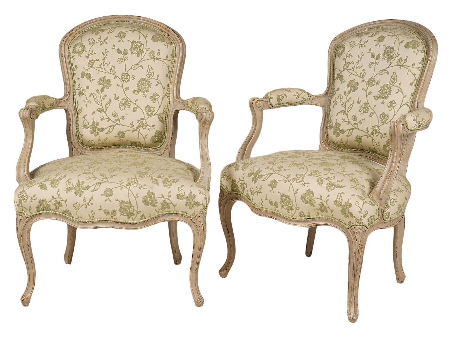 This pair of French Louis XV style armchairs, dating to the early 20th century, feature carved and painted frames, upholstered seats and back rests newly covered with a tasteful fabric.