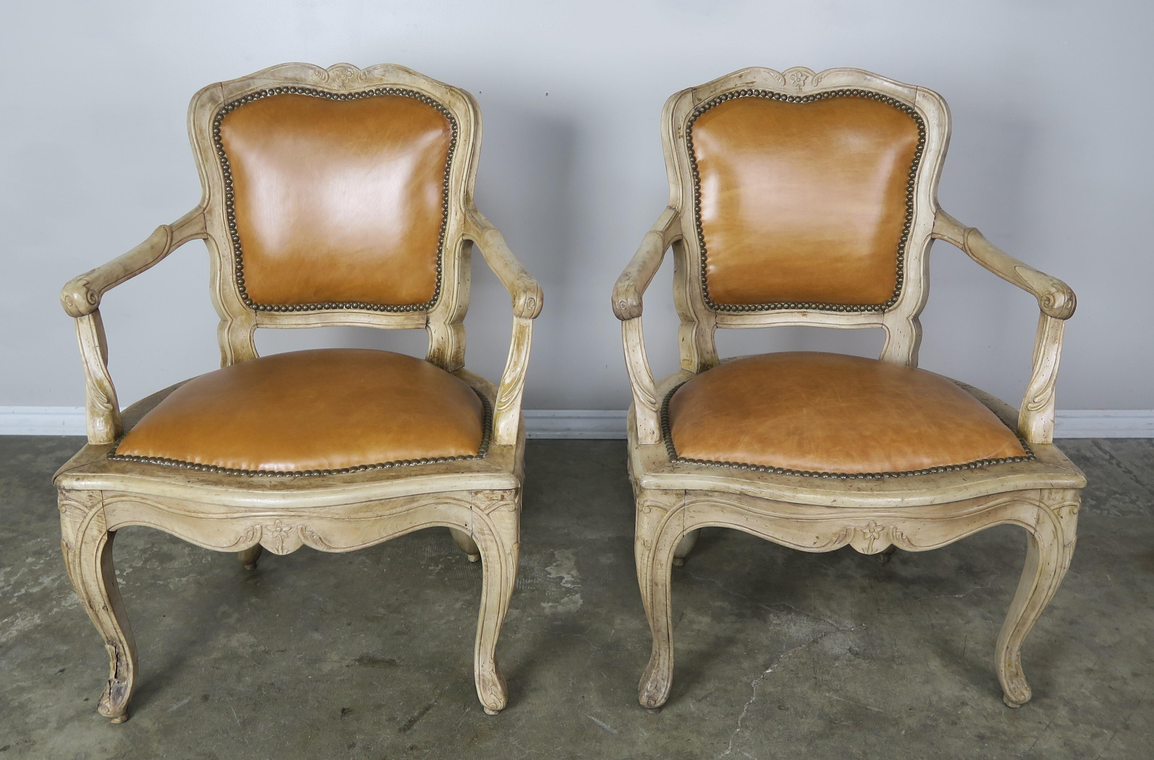Pair of French walnut Louis XV style carved bleached walnut armchairs upholstered in a caramel colored leather with brass nailhead trim detail. The armchairs stand on cabriole legs that end in rams head feet.
Measures: Seat height 17