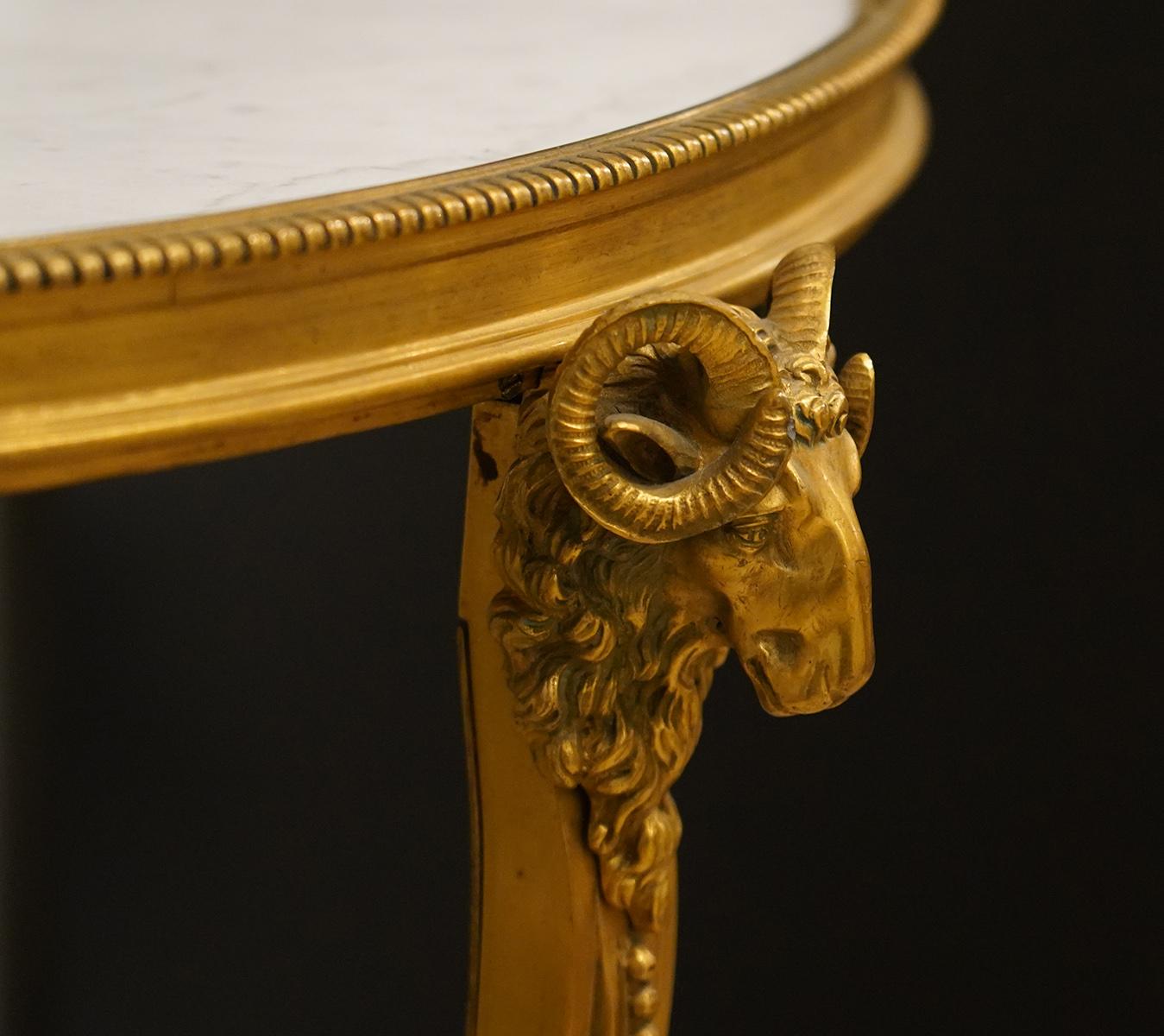 This pair of superior French Louis XV style gilt bronze Guéridon table feature Carrara marble tops set in beaded frames supported by three ram's head adorned gilt bronze cabriole legs ending in foliate hoof feet. The legs are joined by lower marble