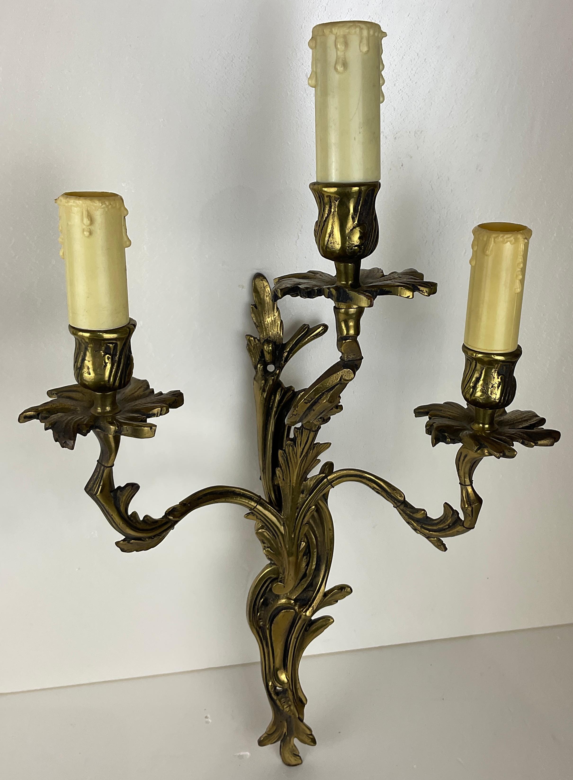 Pair of French Louis XV rococo style gilded bronze double arm wall sconces, in very good antique condition. 
Beautiful decorative floral and leaf tiered scrolling arms. 

Very good quality and well cast.
Electrified.

Dimensions: 5 3/4