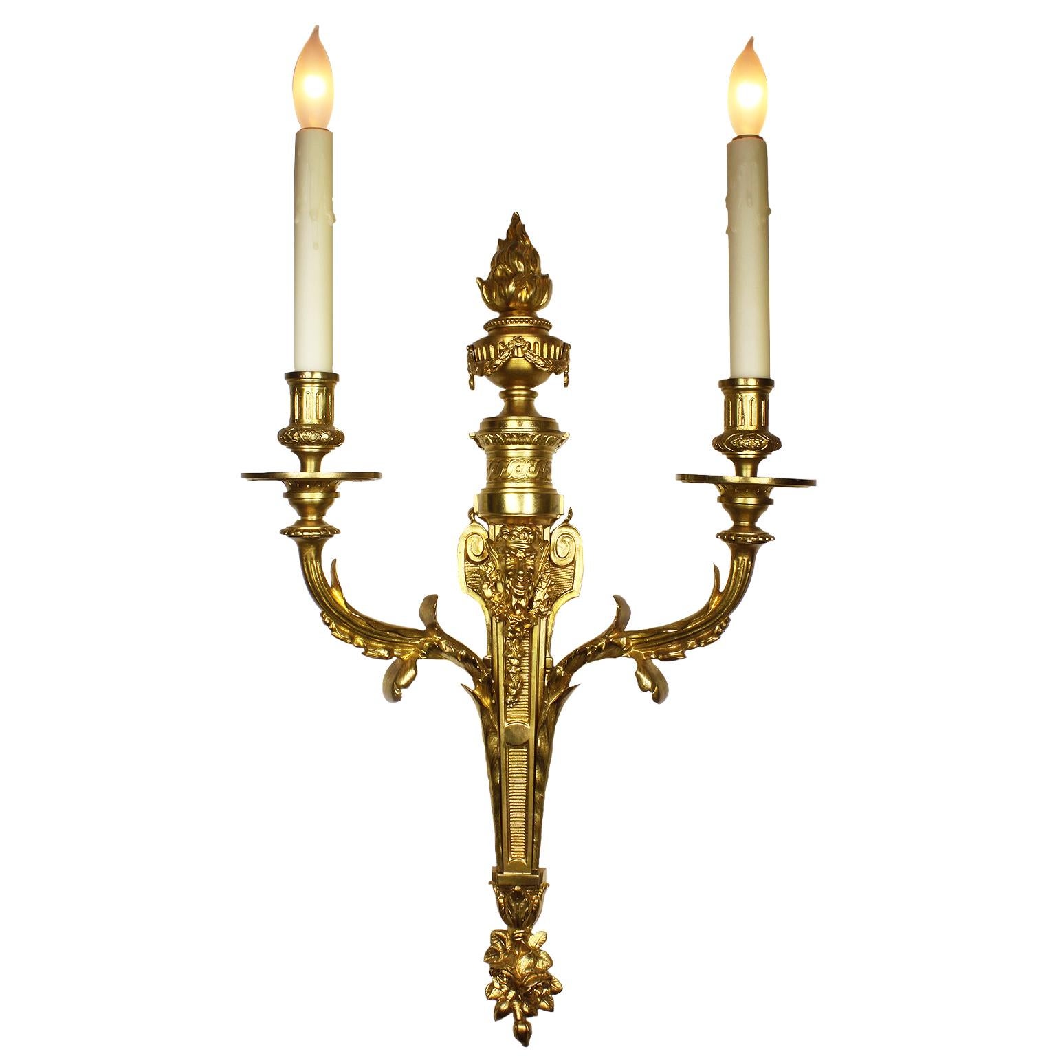 A fine pair of French 19th century Louis XV style gilt-bronze two-light wall light sconces. The slender tapered body surmounted with a mask figure of Bacchus above a pair of scrolled candle-arms and crowned with a flambeaux urn with a burning flame,