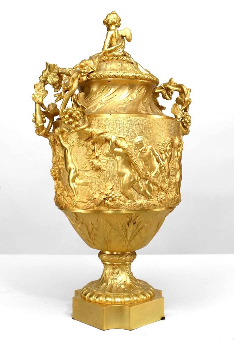 Pair of French Louis XV style gilt bronze urns with cupid in relief and twig and grape design handles with cupid finial top (19th Century).
 