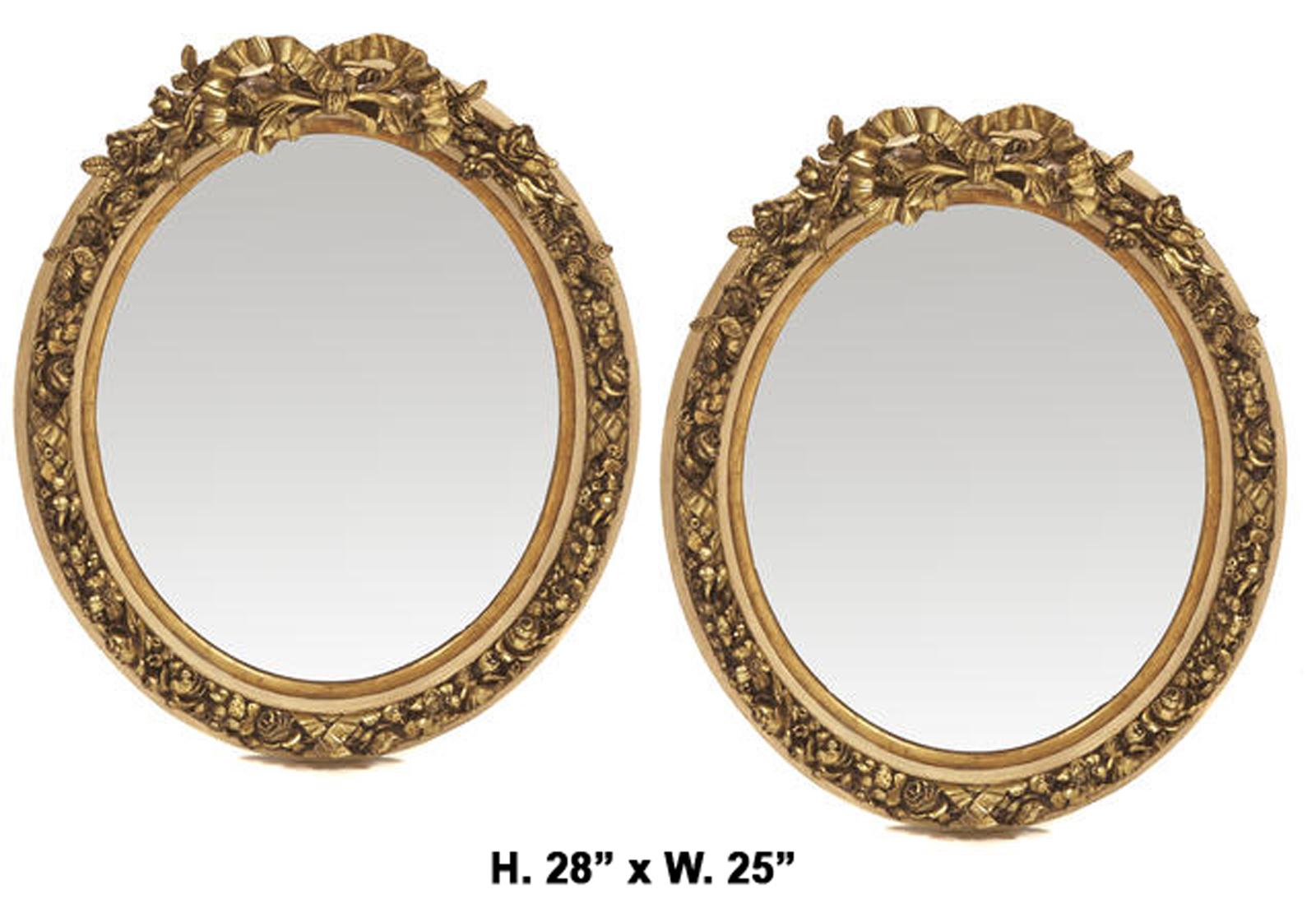 Paire de miroirs ovales dorés de style Louis XV français.
Milieu du 20e siècle. 

Les miroirs sont surmontés d'un ruban doré sculpté, chacun étant décoré d'un motif de fruits, de fleurs et de feuillages, le cadre festonné entourant une plaque de