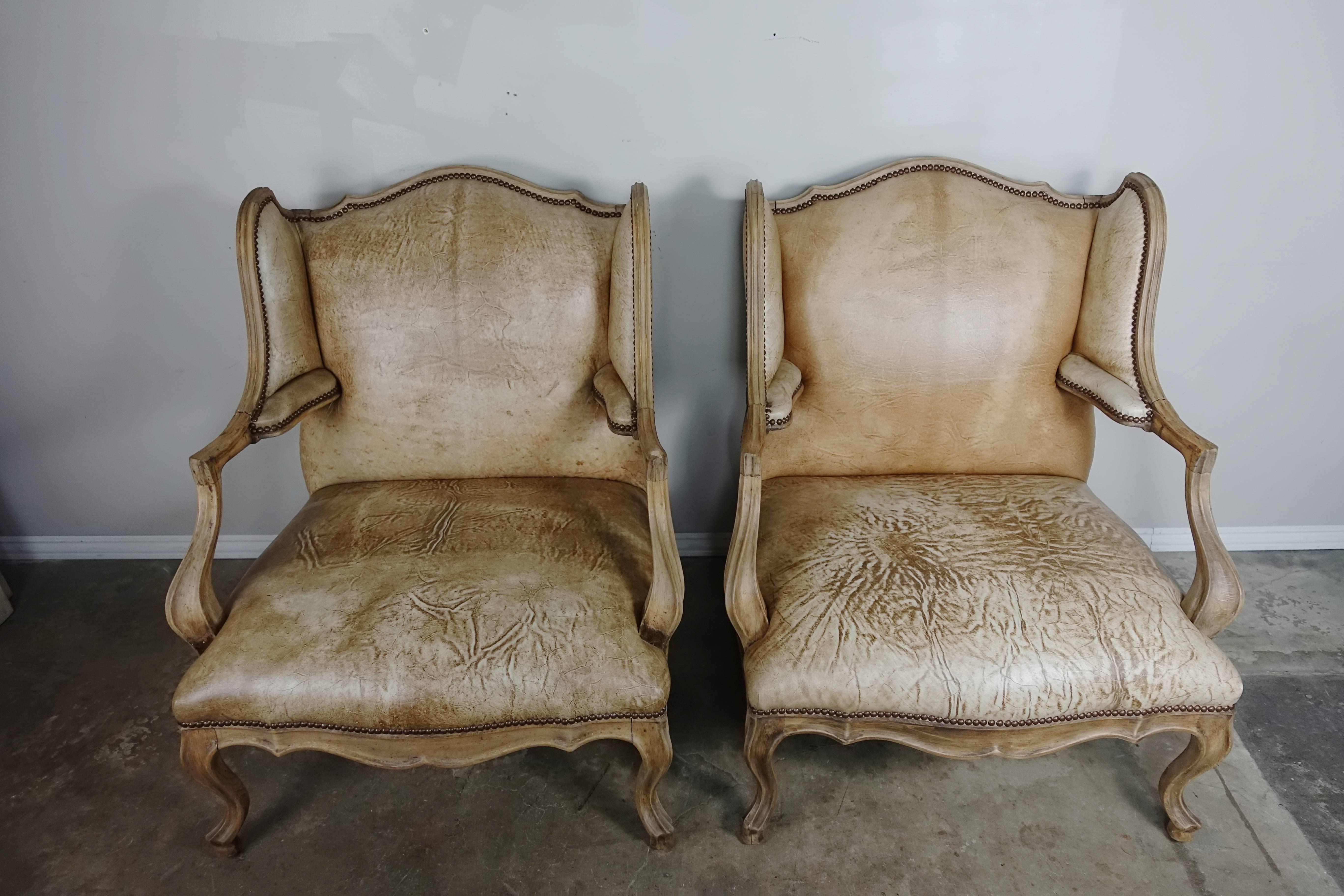 Pair of Antique French Louis XV style wingback Leather armchairs upholstered in unique distressed cow hides with nailhead trim detail.