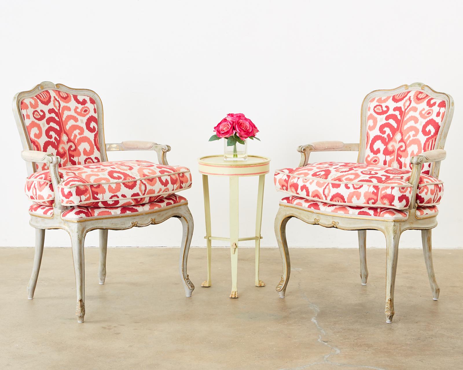 Fabulous pair of French fauteuil armchairs featuring an ikat design modern upholstery in coral pinks and reds. Made in the grand Louis XV style with lacquered frames having a parcel gilt finish and a beautifully aged patina on the lacquer. Padded