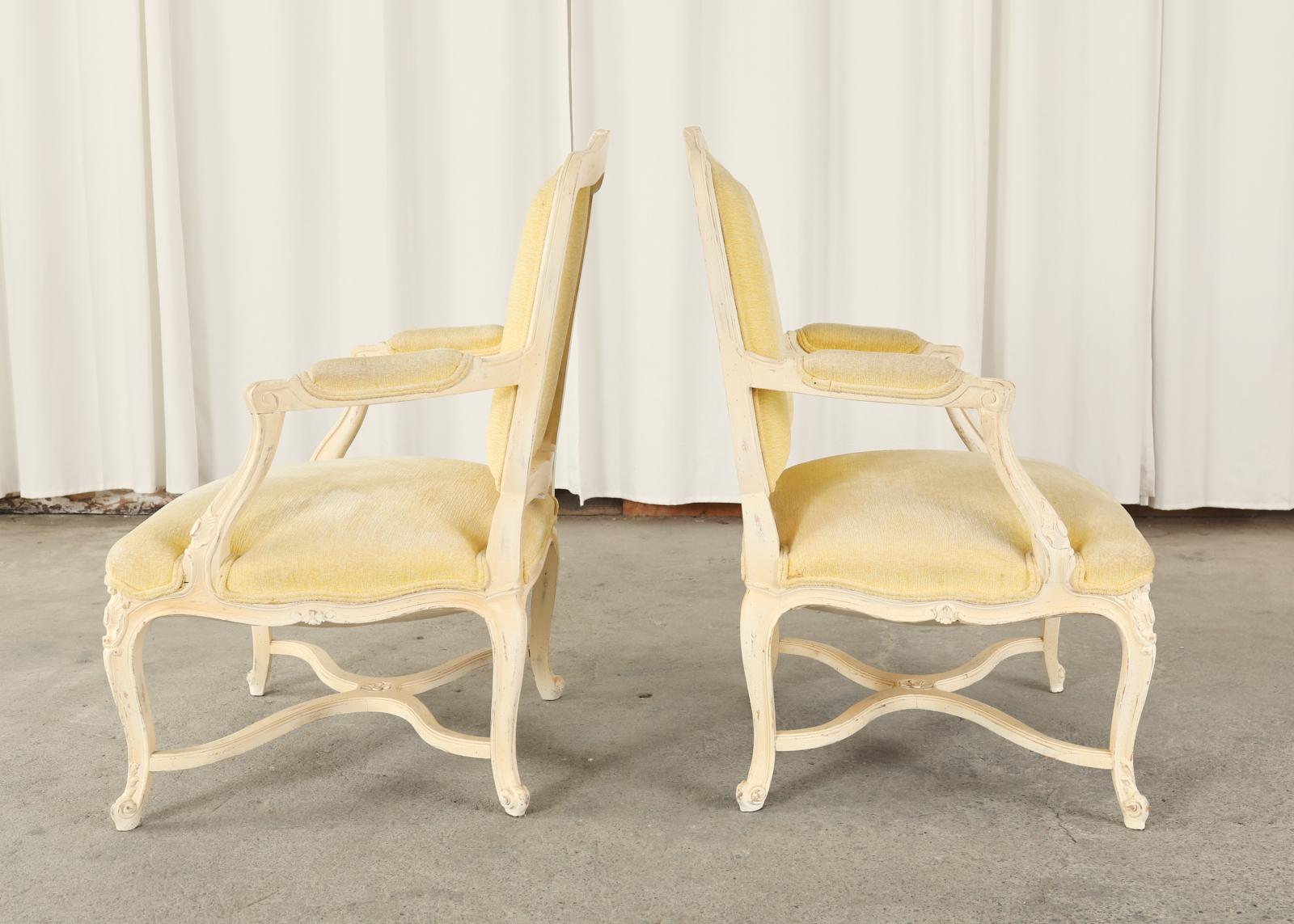 Country French provincial or Louis XV style pair of painted fauteuil armchairs. The set features a generous seating area with a vintage butter colored velvet upholstery. The frames have a large square back with molded arms and a serpentine seat
