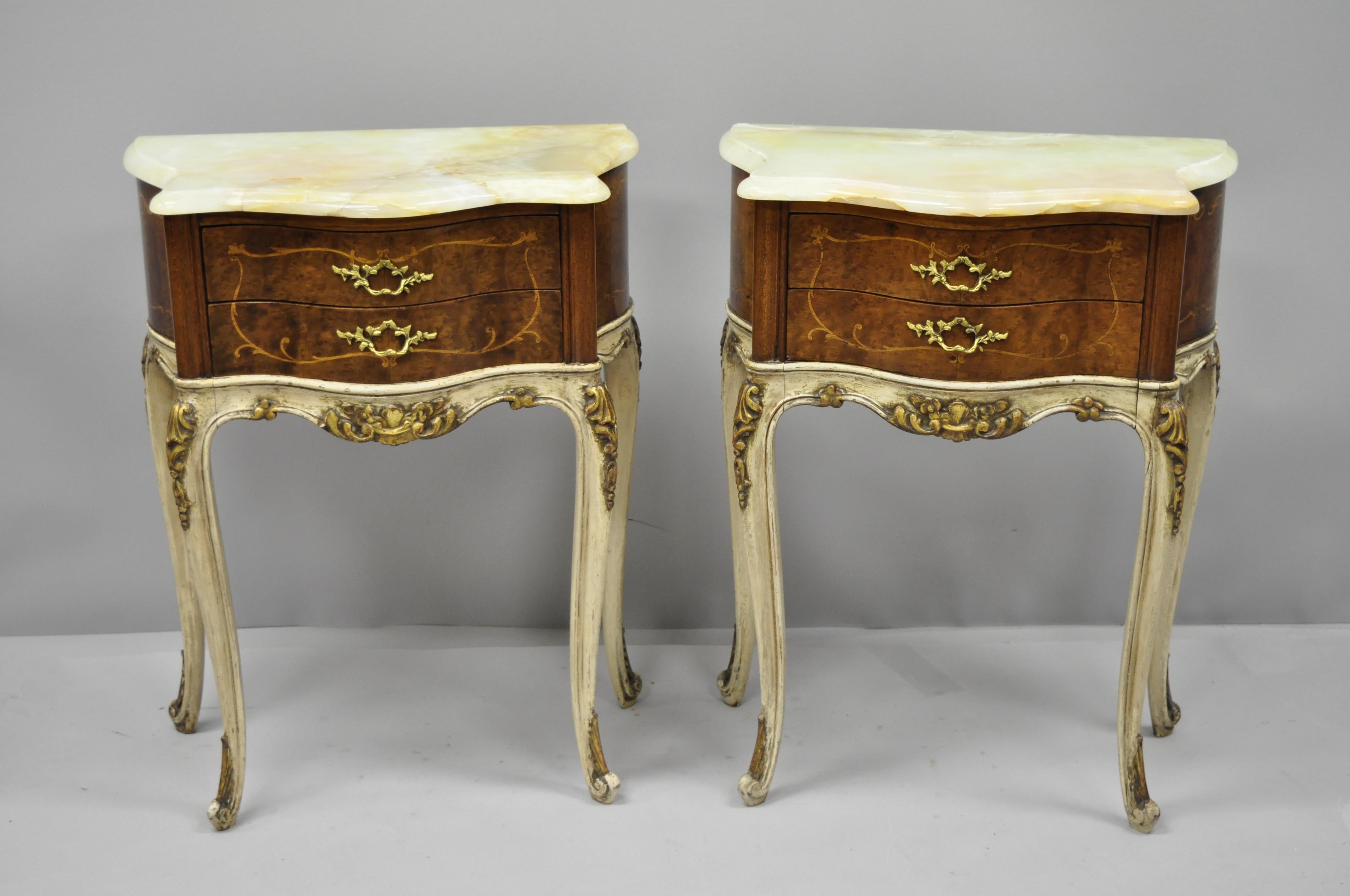 Pair of antique French Louis XV style small onyx top inlaid bombe nightstands. Item features shaped onyx stone tops, nice petite from, bombe shaped base, inlaid drawer fronts, and sides, cream and gold distressed painted, circa early 20th century.