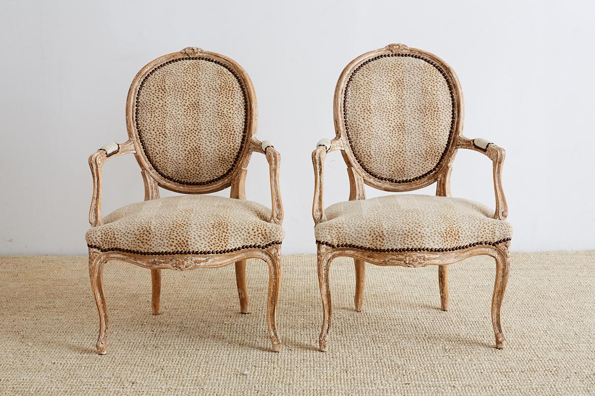 Fabulous pair of French Louis XV style carved fauteuil armchairs. Featuring an animal print upholstery with a linen inset in the exposed back. The frames have floral carved crests and aprons with molded arms and legs. The upholstery is bordered with
