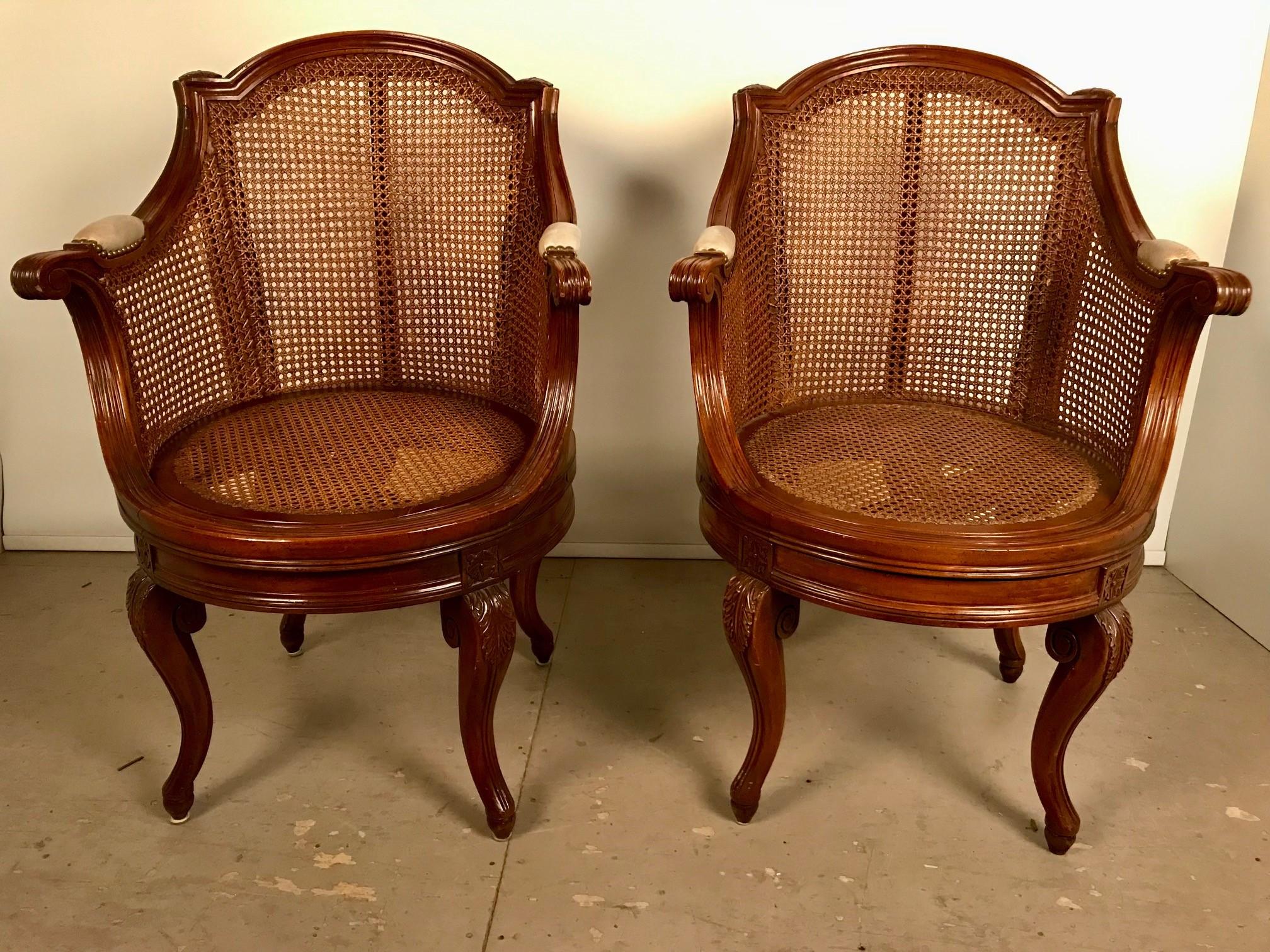 A Pair of French Louis XV style walnut swivel armchairs, the caned seats and back are in excellent condition. These are a wonderful and quite comfortable pair, with a curved back back paterae and leather padded over carved arms, supported on French